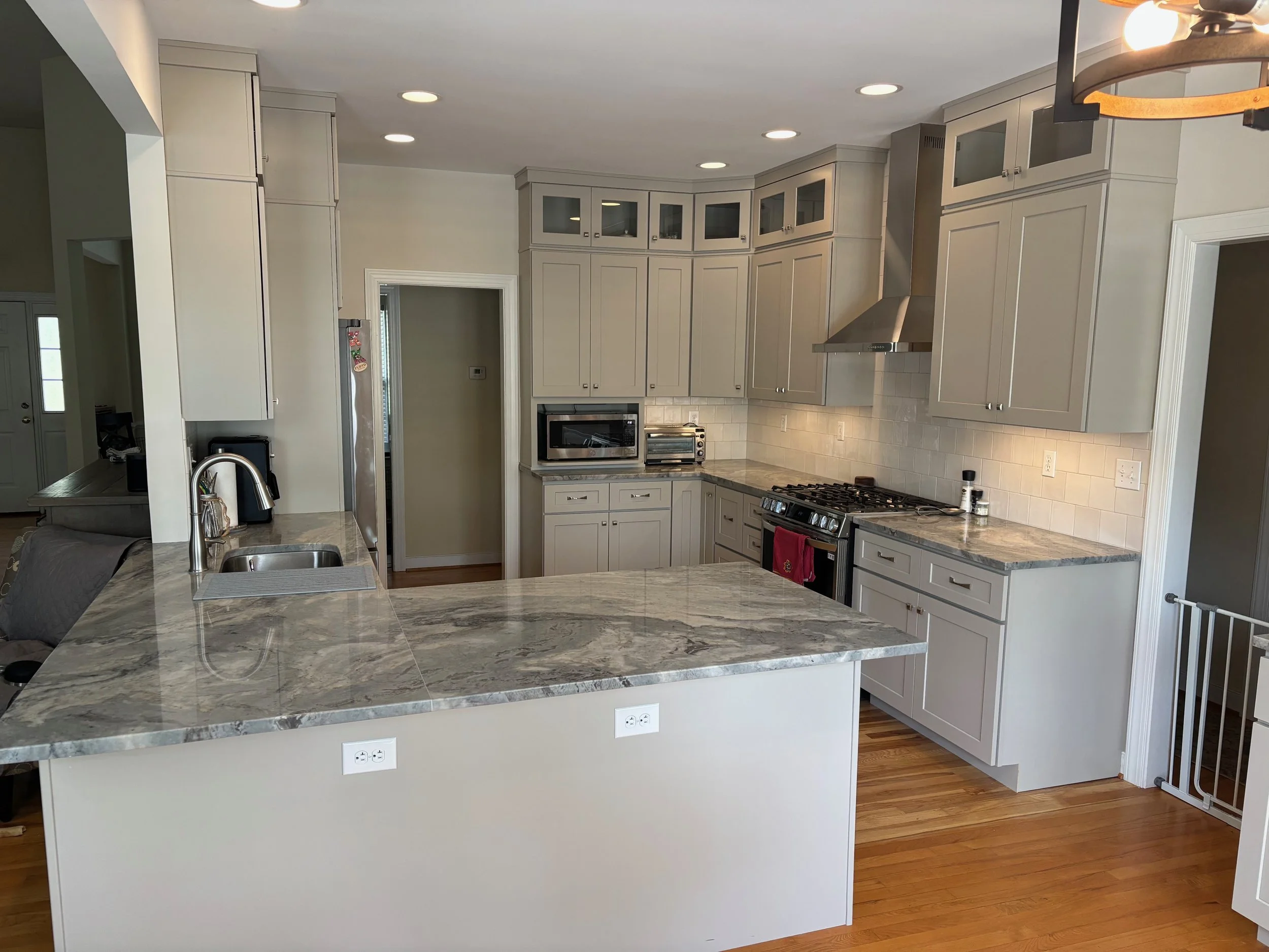 Modern kitchen with white cabinets, marble countertops, stainless steel appliances, and hardwood flooring.