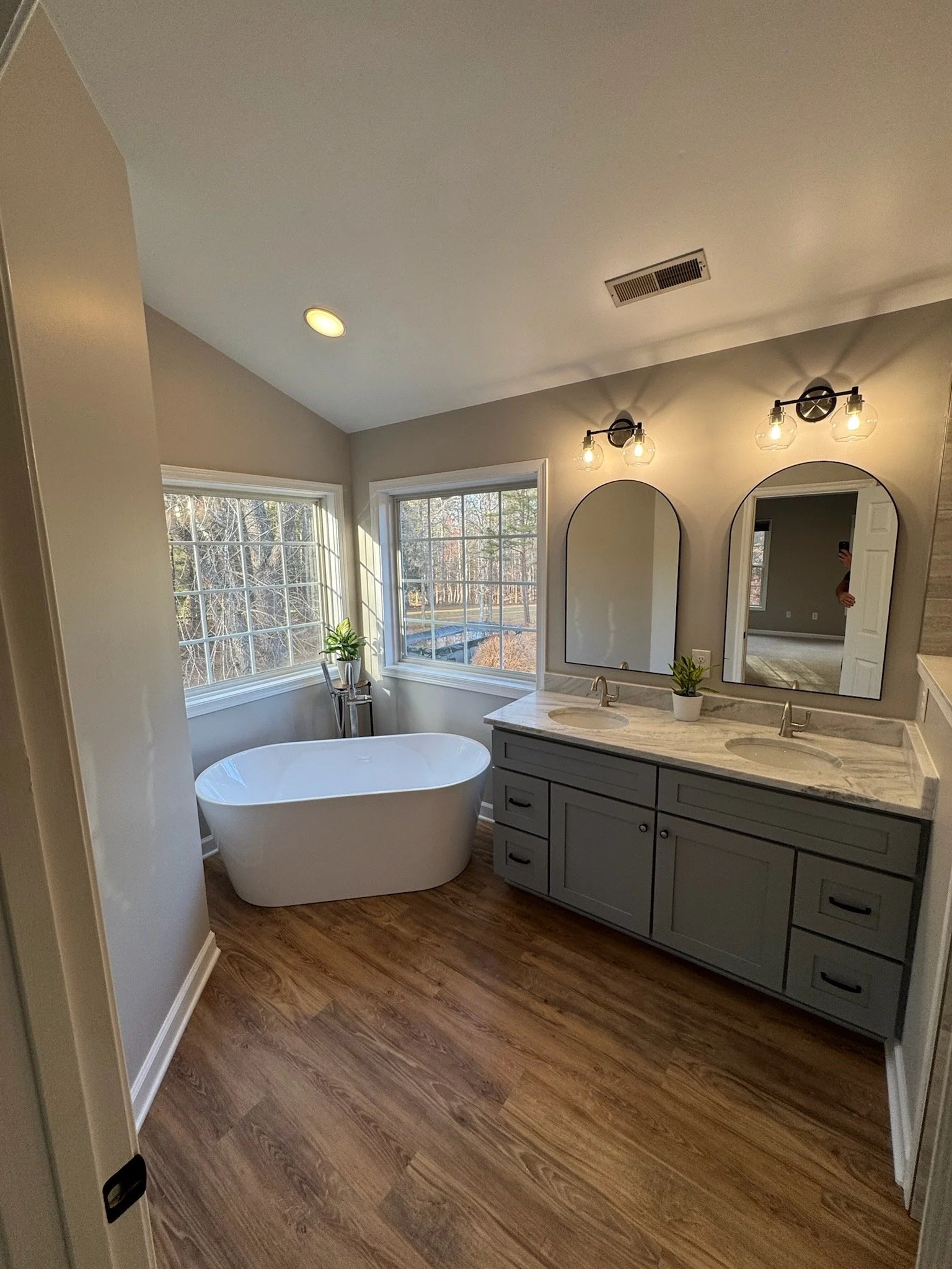 Bathroom with large windows, a freestanding bathtub, a double vanity with two sinks, mirrors, and modern lighting fixtures.