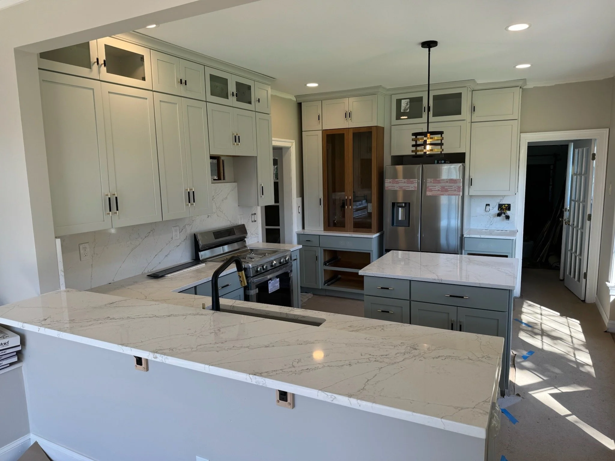 Newly renovated kitchen with white and wood cabinets, marble countertops, stainless steel appliances, and pendant lighting.