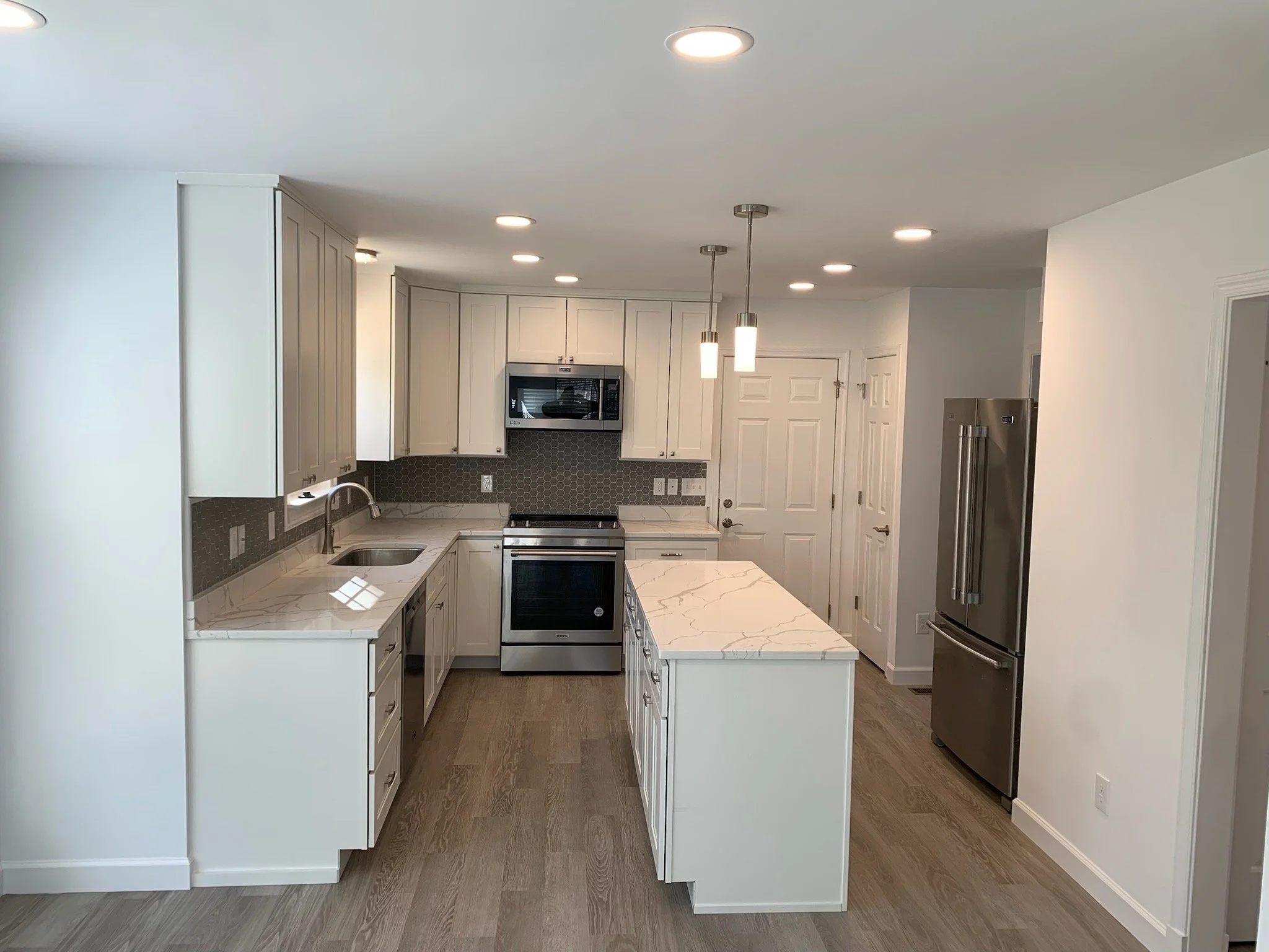 Modern kitchen with white cabinets, a stainless steel refrigerator, black hexagon tile backsplash, marble countertops, and hanging pendant lights.