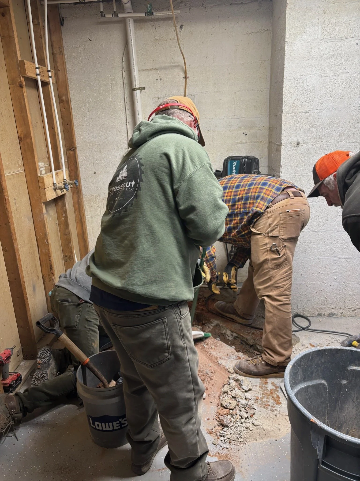 Workers inside a construction site working on the foundation or plumbing of a building, surrounded by construction tools and debris.
