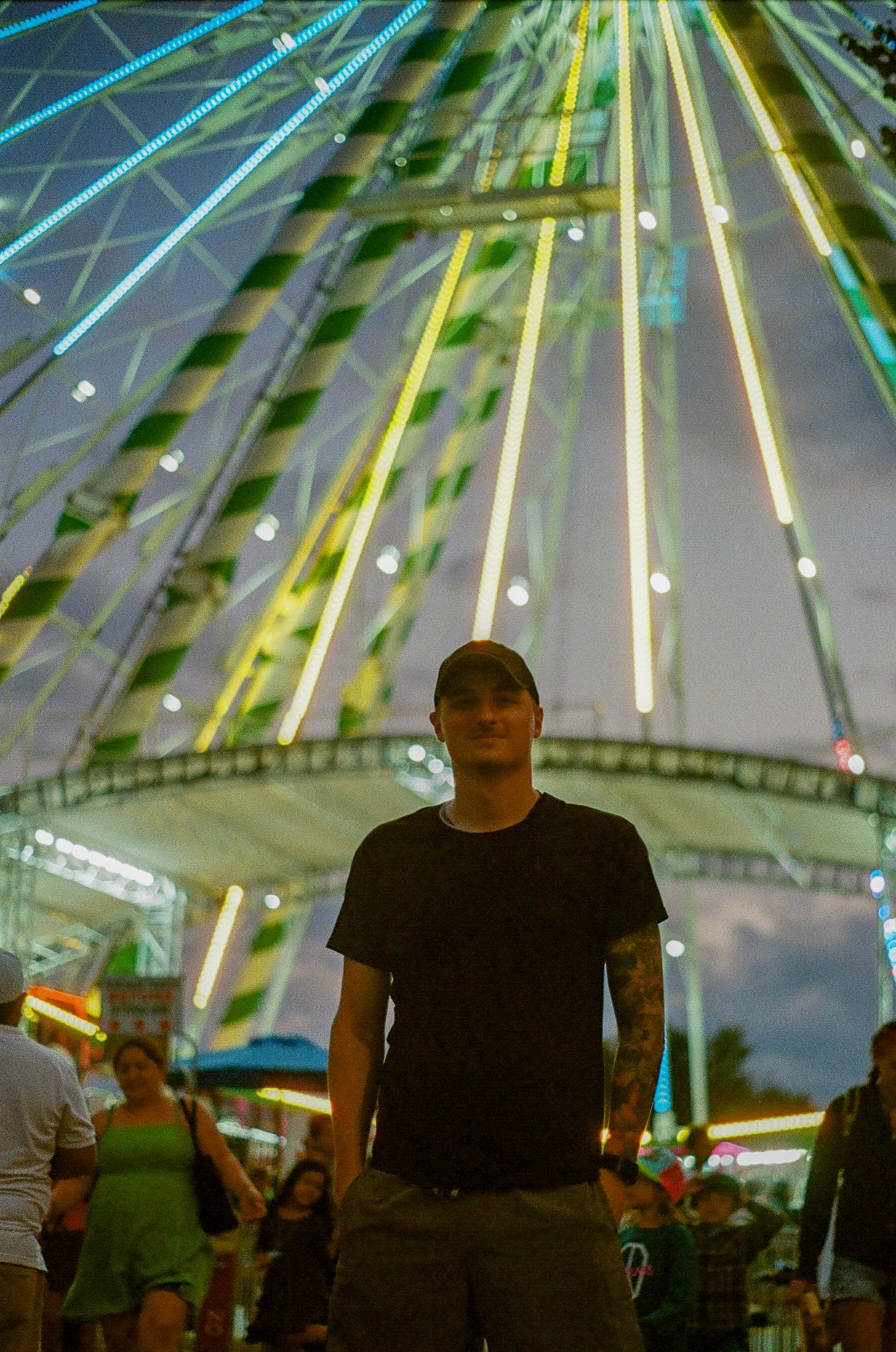 A person standing in front of a brightly lit amusement park ride at night.