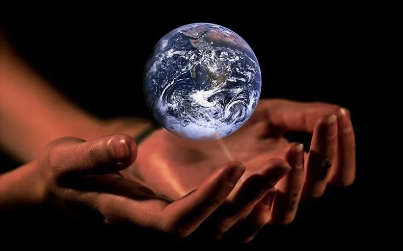 A pair of human hands gently cradling a small, glowing Earth against a dark background.
