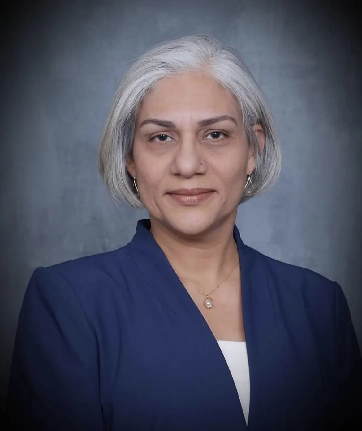 A middle-aged woman with shoulder-length gray hair wearing a white turtleneck sweater against an orange background.