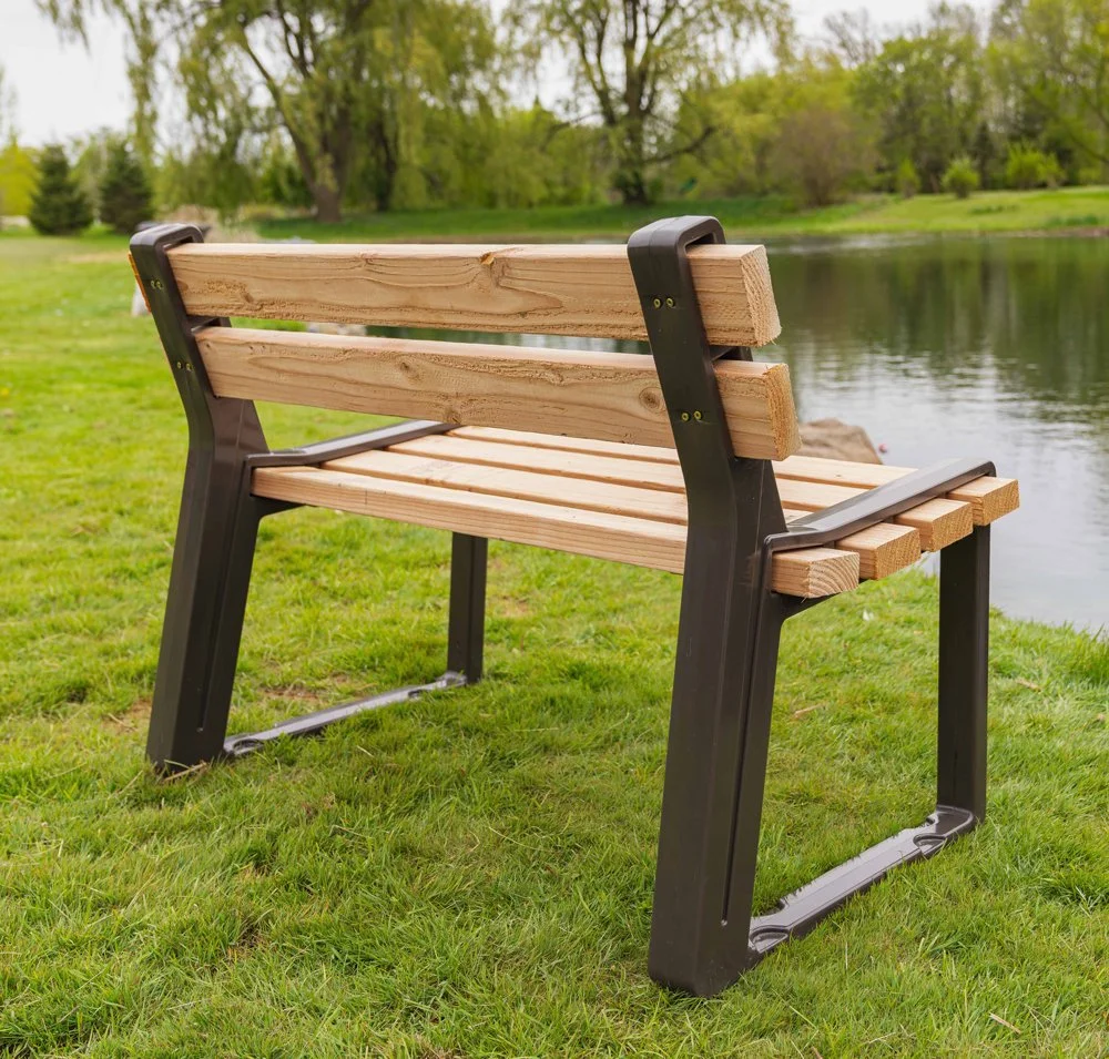 A wooden park bench with black metal legs, positioned on a grassy area near a lake with trees in the background.