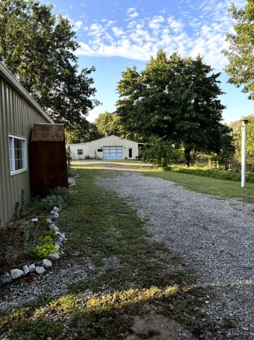Gravel driveway leading to white garage building surrounded by trees on a country property.