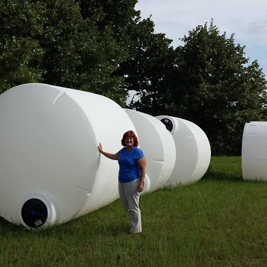 Tchinina is standing next to large, white, cylindrical tanks outdoors.