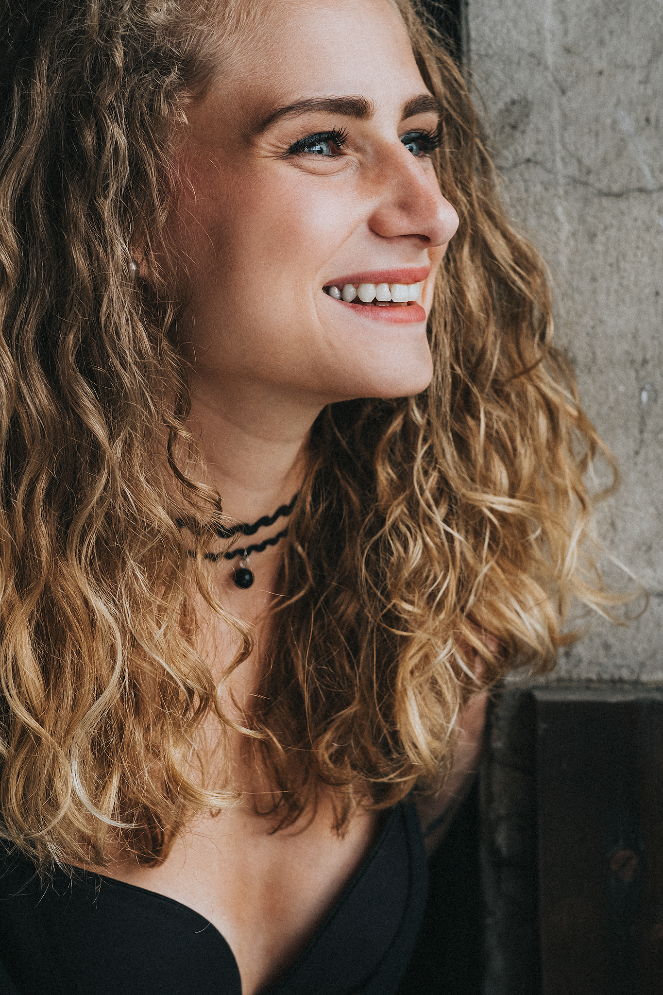 Lächelnde Frau mit lockigem blondem Haar, die zur Seite schaut.