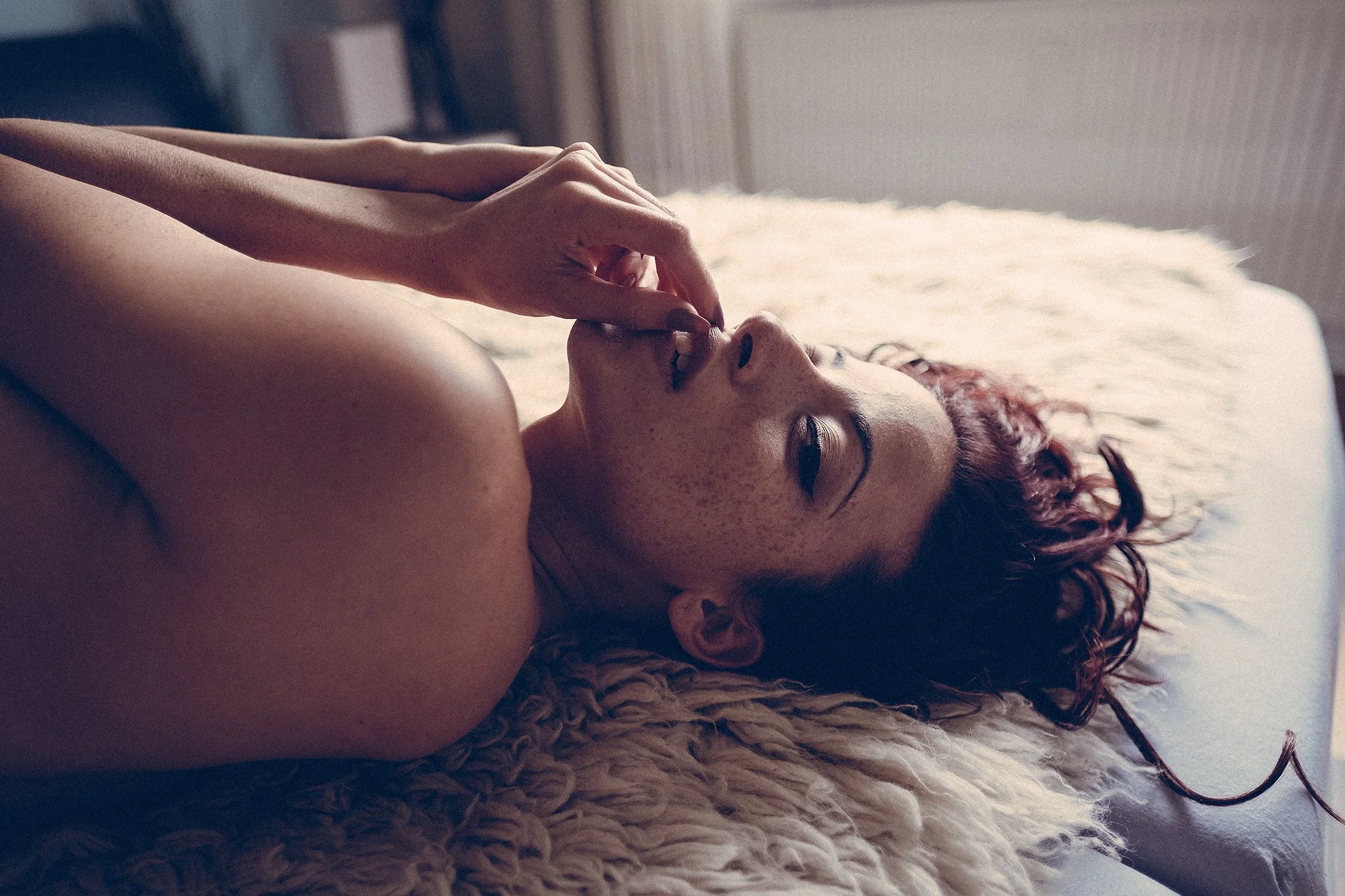 Frau mit roten Haaren liegt auf einem Fellteppich.