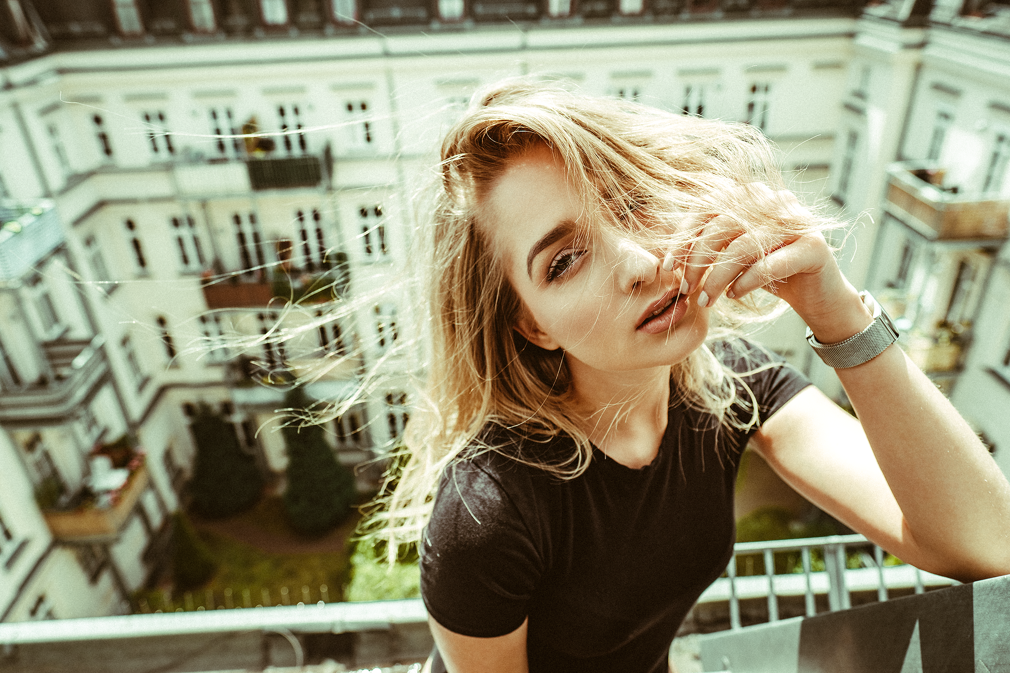 Junge Frau mit wehenden Haaren auf einem Balkon stehend, mehrstöckiges Gebäude im Hintergrund.