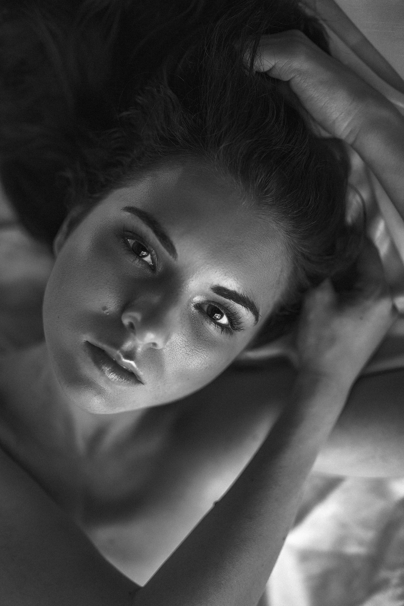 Schwarz-weiß-Fotografie einer Frau, die auf dem Rücken liegt, mit den Händen in den Haaren.