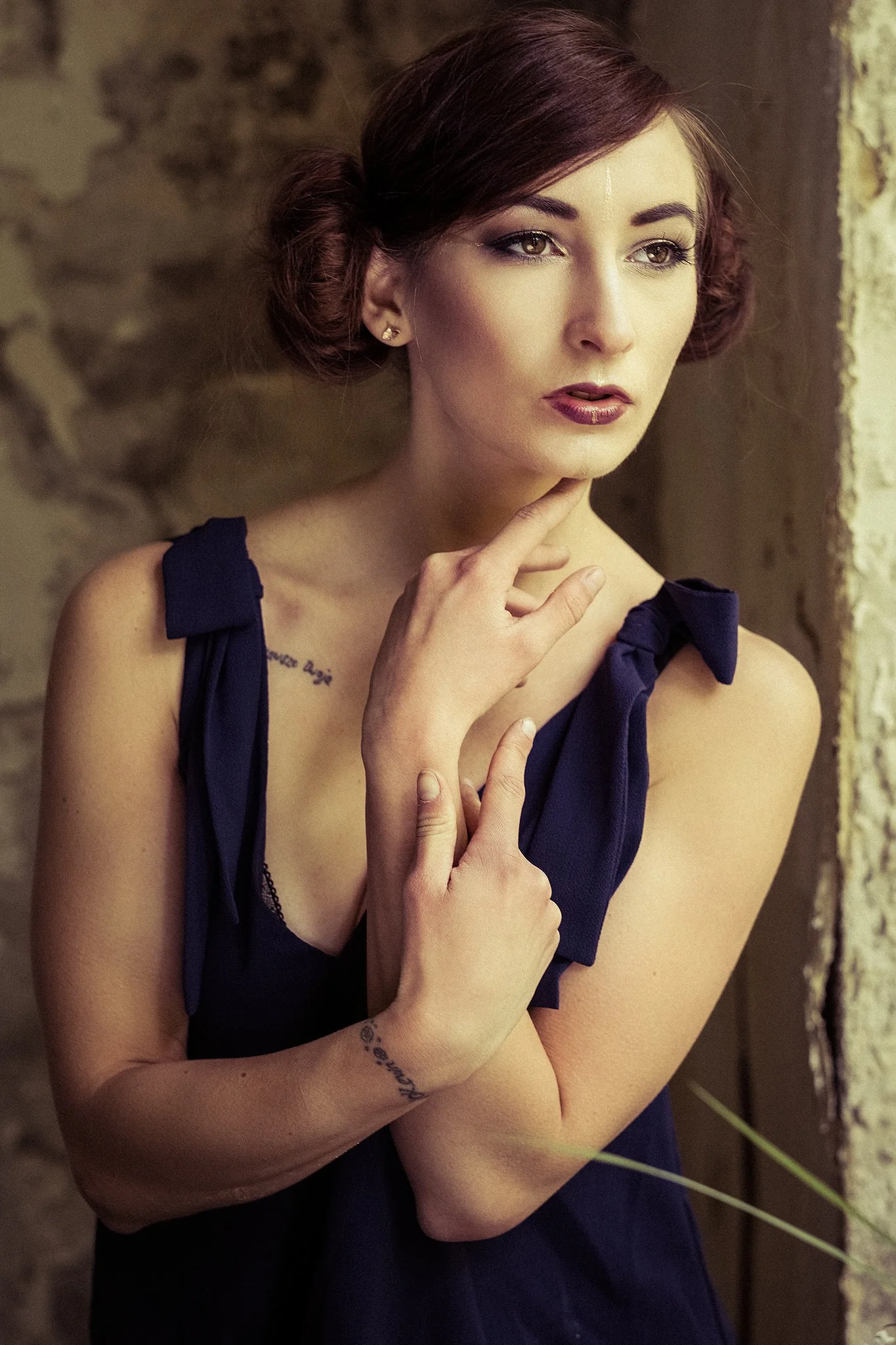 Porträt einer Frau mit dunklem, hochgestecktem Haar, die ein dunkles Kleid trägt und nachdenklich aus einem Fenster schaut.