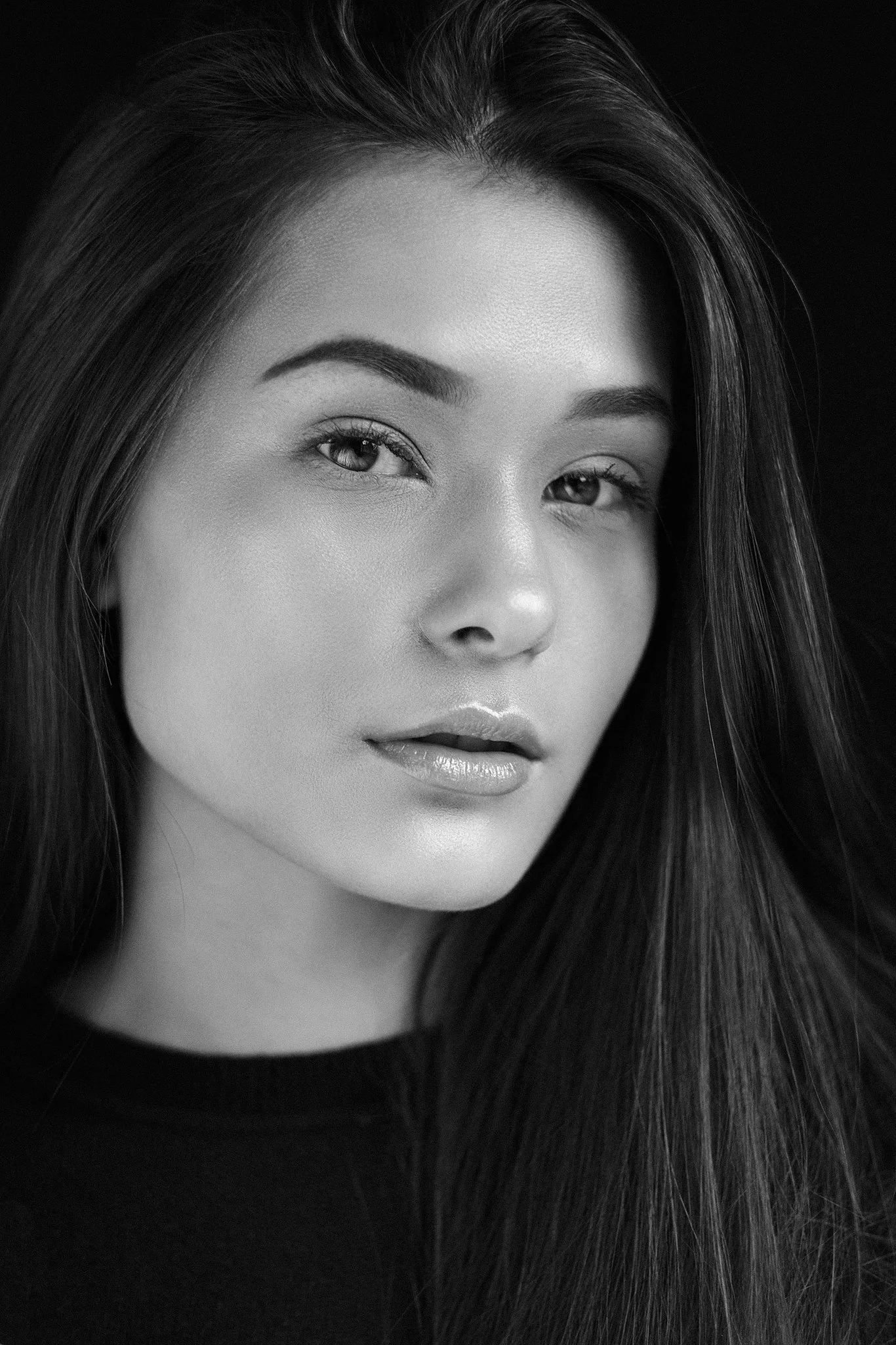 Nahaufnahme eines Gesichts einer Frau in Schwarz-Weiß, mit glattem Haar und neutralem Ausdruck.
