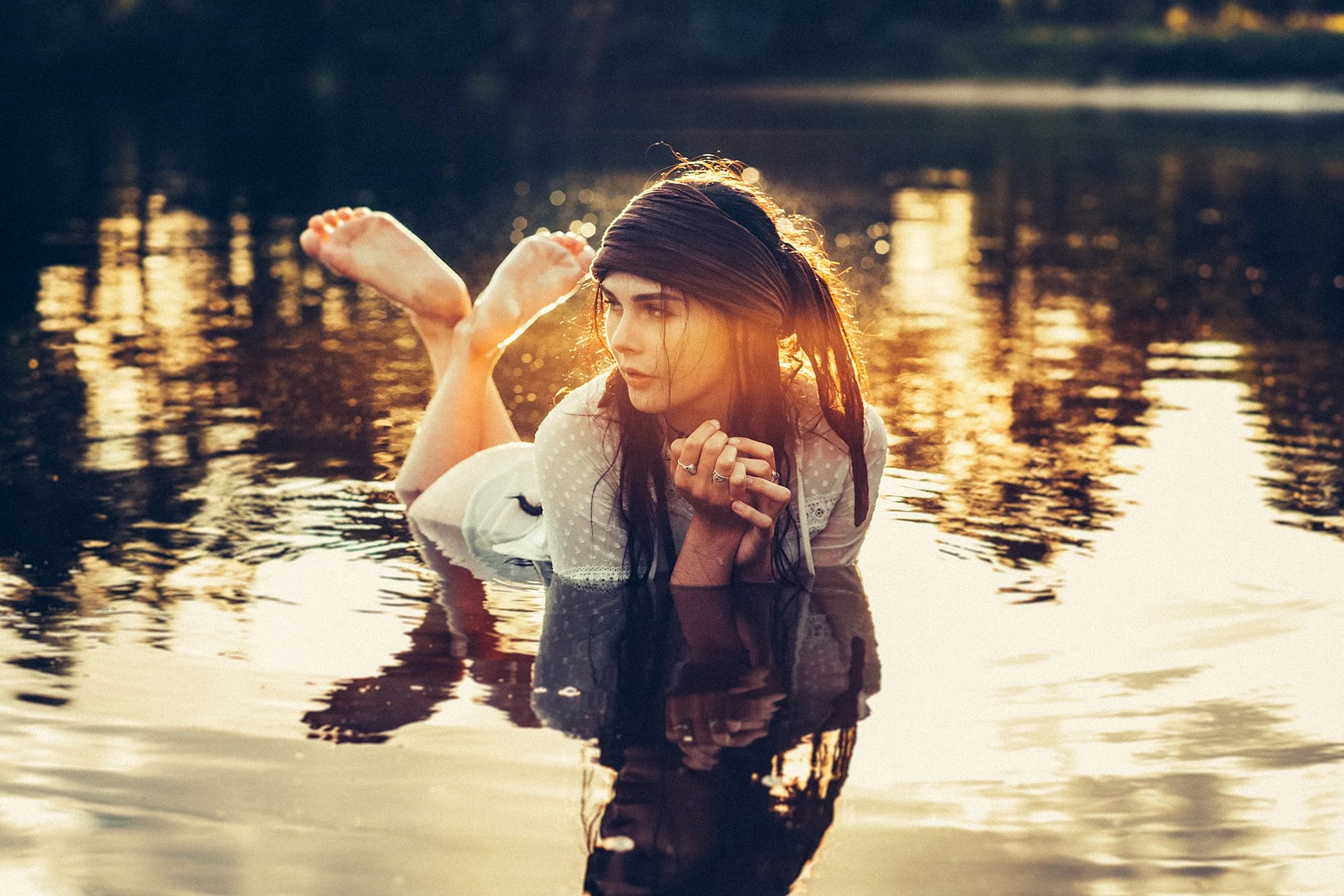 Frau mit Kopftuch liegt im flachen Wasser, Sonnenuntergang spiegelt sich.