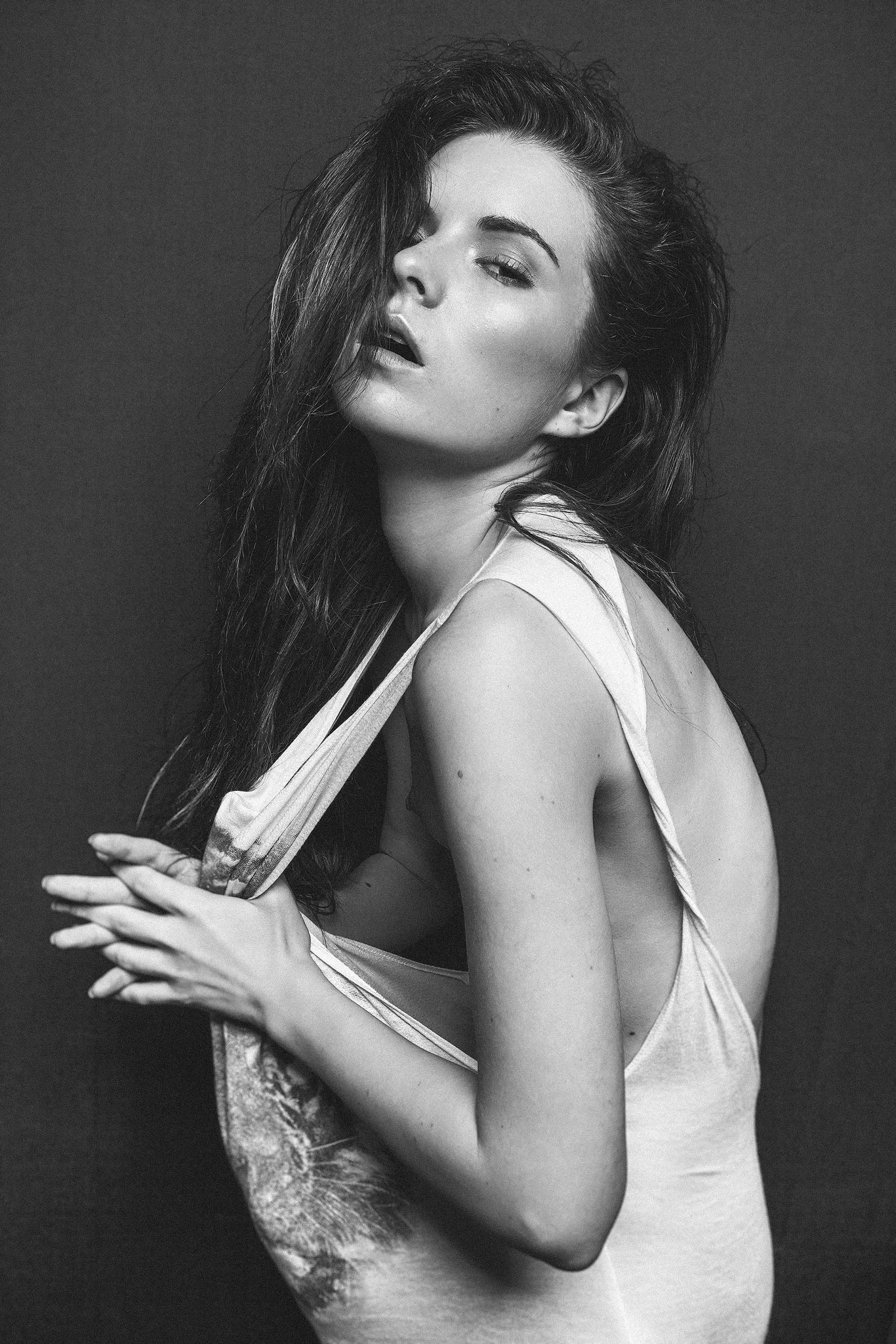 Schwarz-weiß-Foto einer Frau in einem weißen Oberteil, die eine sinnliche Pose einnimmt. Sie hat langes, dunkles Haar und schaut in die Kamera.