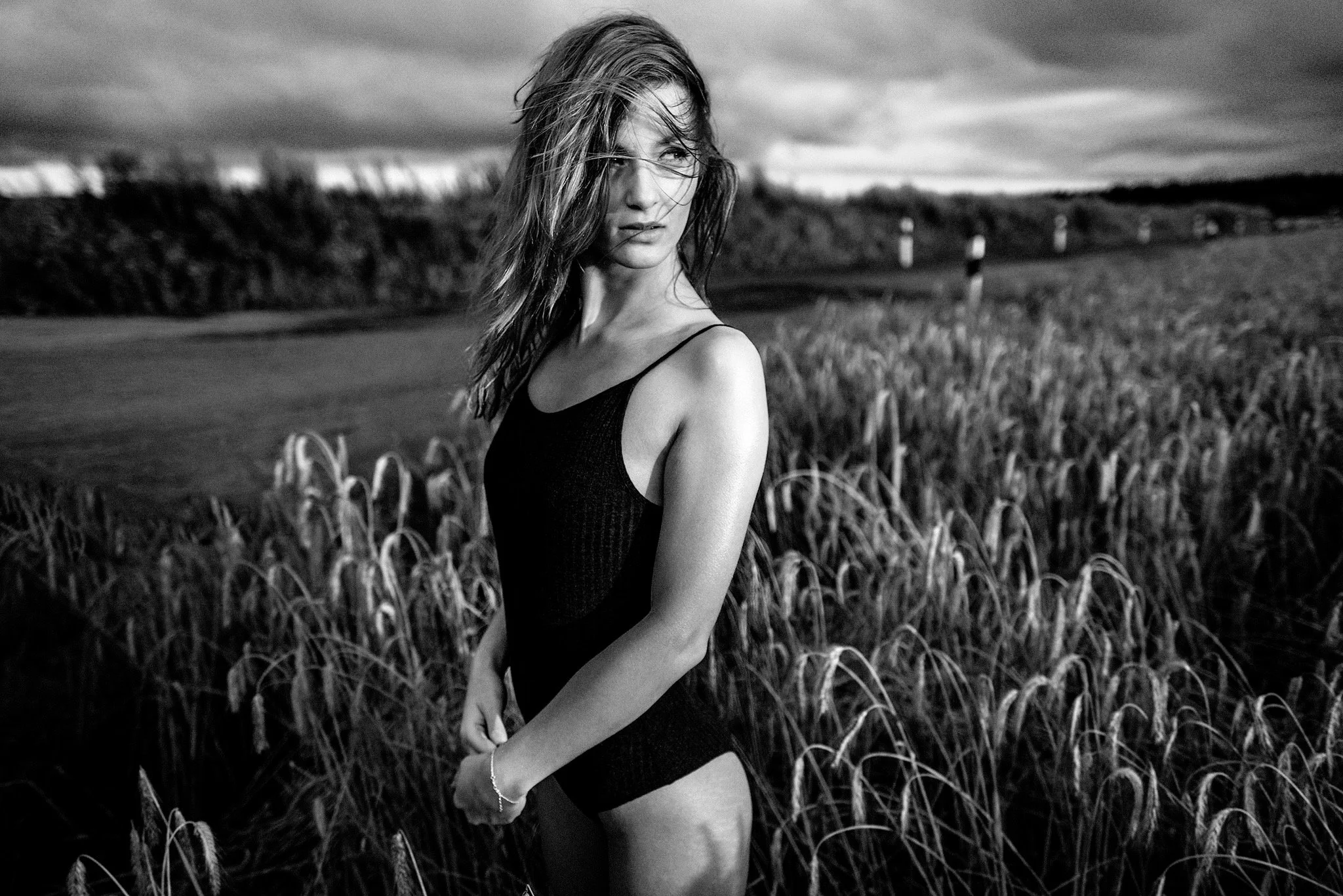 Schwarz-weiß Foto einer Frau in Badebekleidung, die in einem Feld mit hohem Gras steht.