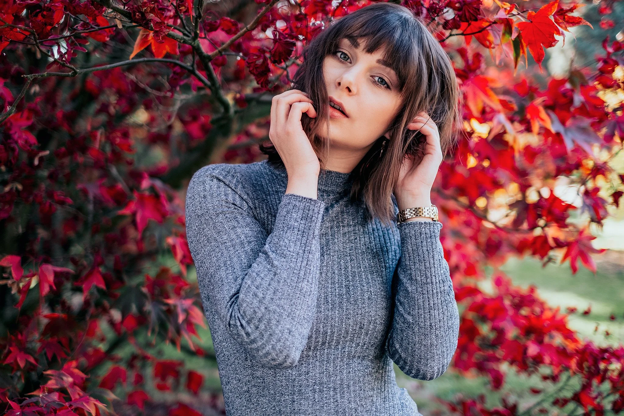 Frau im grauen Pullover steht vor einem Baum mit roten Blättern, Herbststimmung