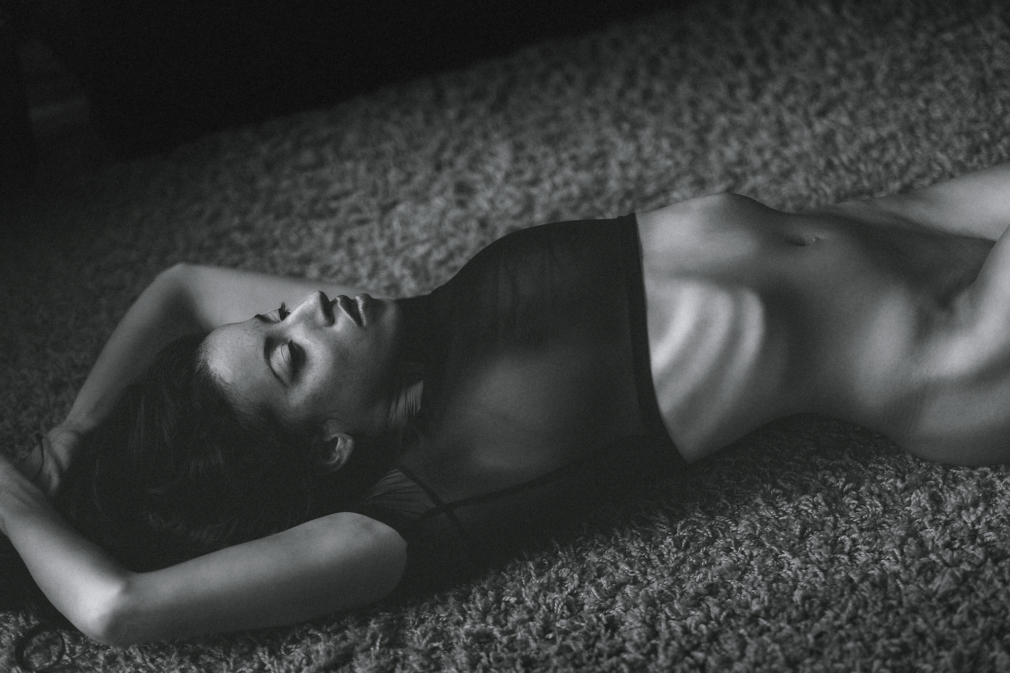 Eine schwarz-weiße Aufnahme zeigt eine Person, die auf einem Teppich liegt, mit den Armen hinter dem Kopf verschränkt.