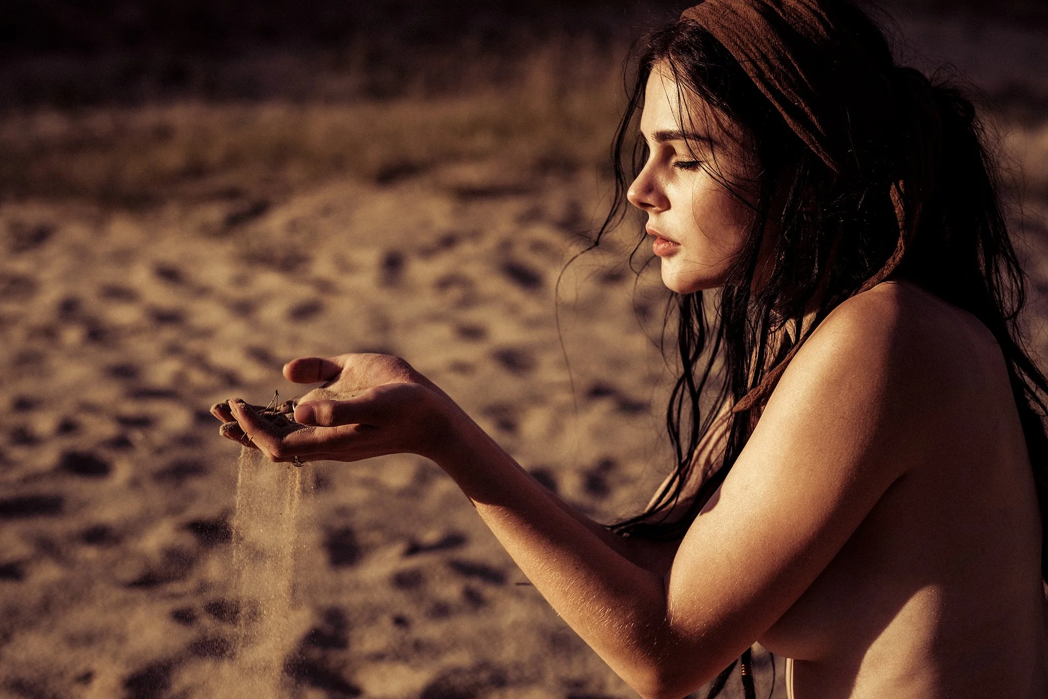 Frau hält Sand in der Hand, Sonnenlicht, Sandstrand im Hintergrund.