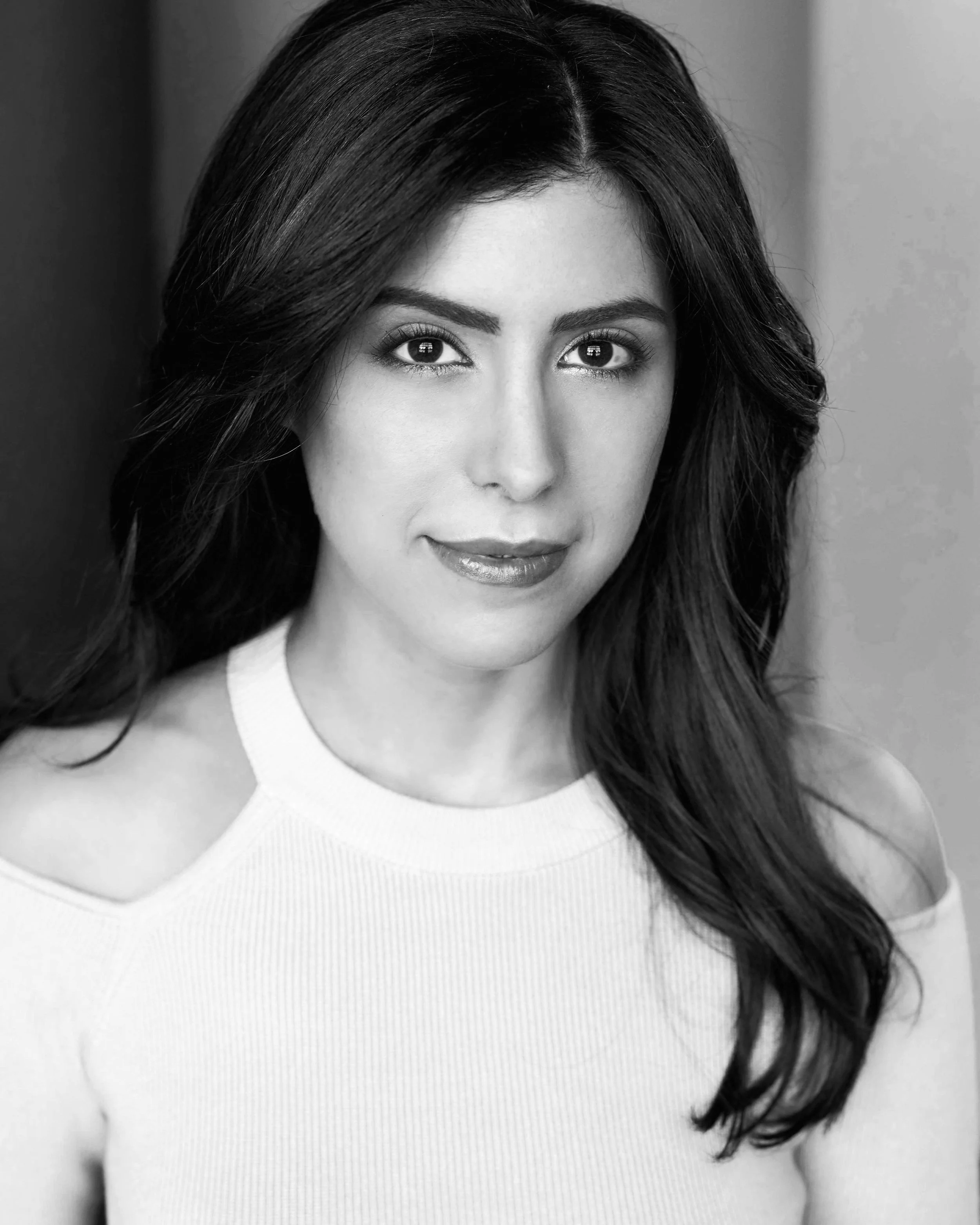 Black and white portrait of a woman with long dark hair wearing a light-colored sweater with cut-out shoulders.