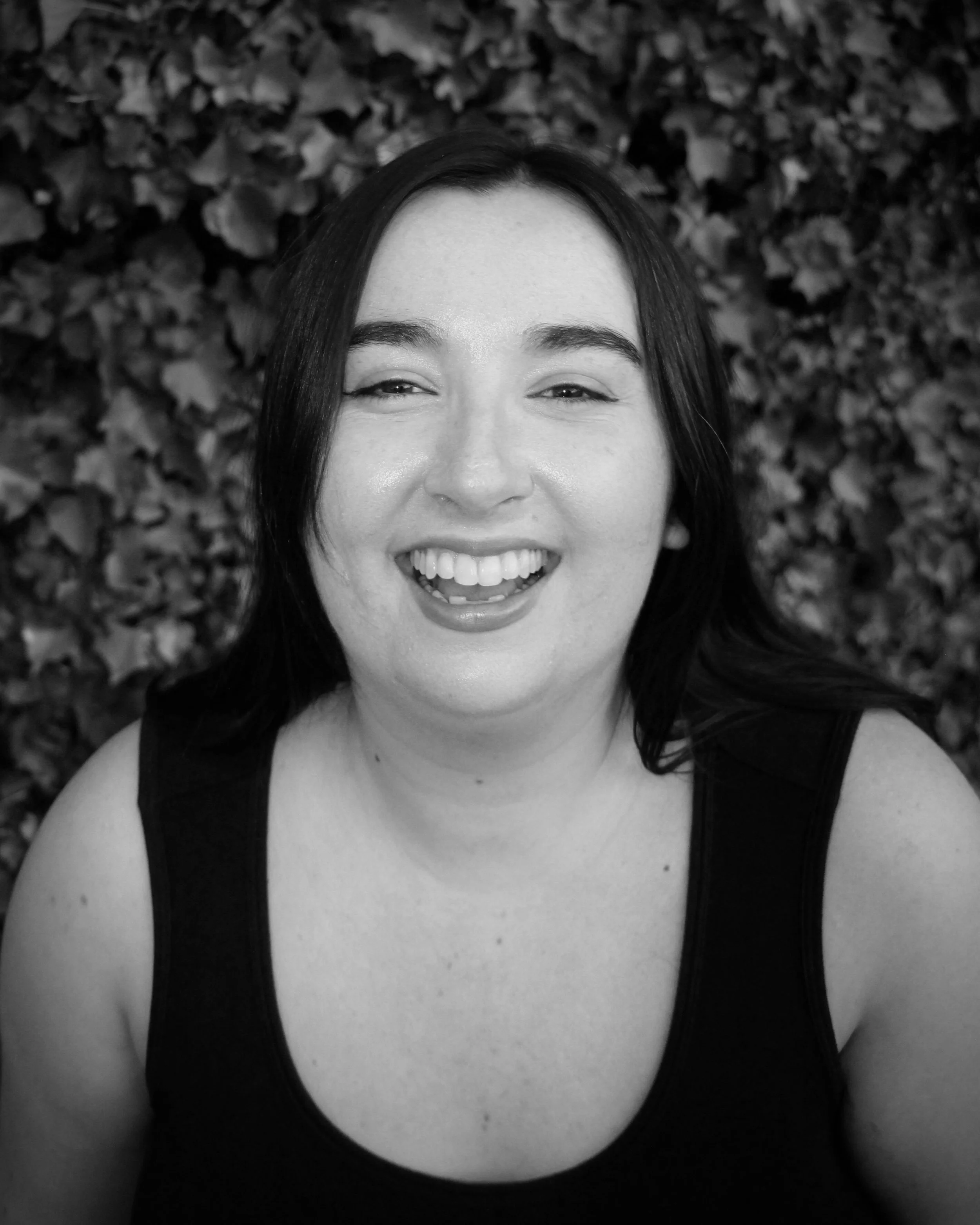 Smiling person in black and white with a leafy background.