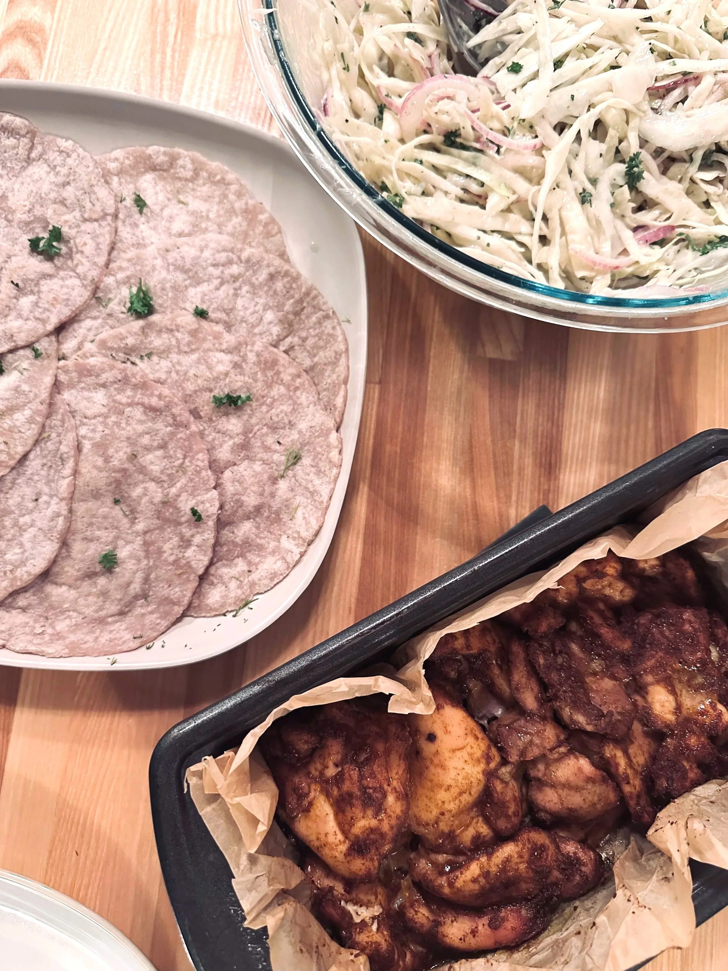 An image of a plate of flatbreads, a pan of spicy chicken and a blow of cabbage slaw