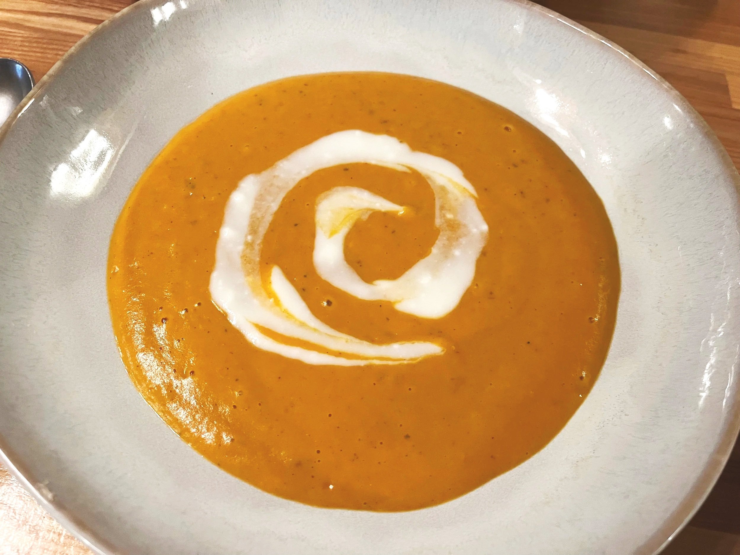 An image of a white bowl with an orange soup with a white cream swirl