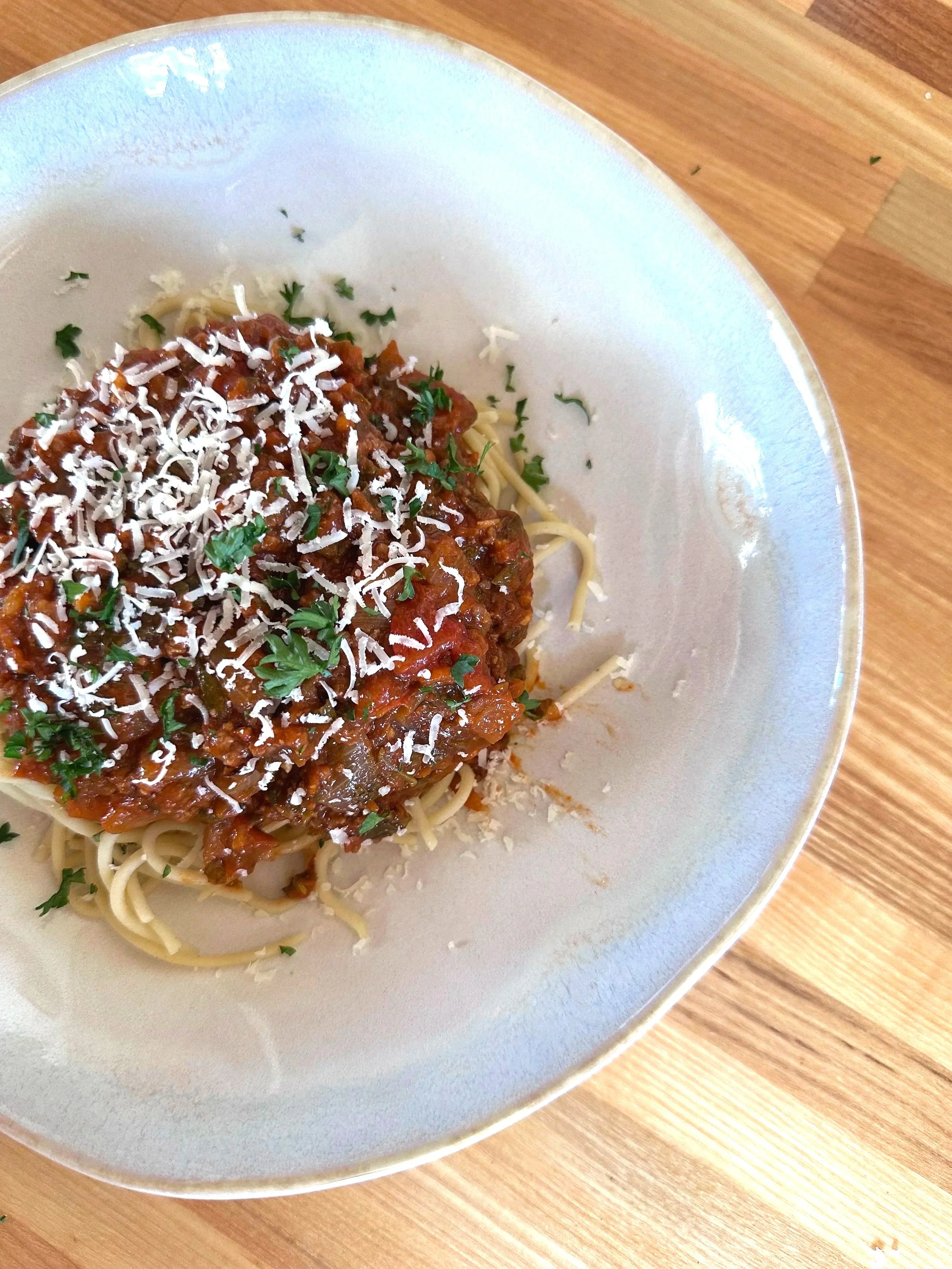 An image of spaghetti with red sauce, shaved cheese and parsley on top