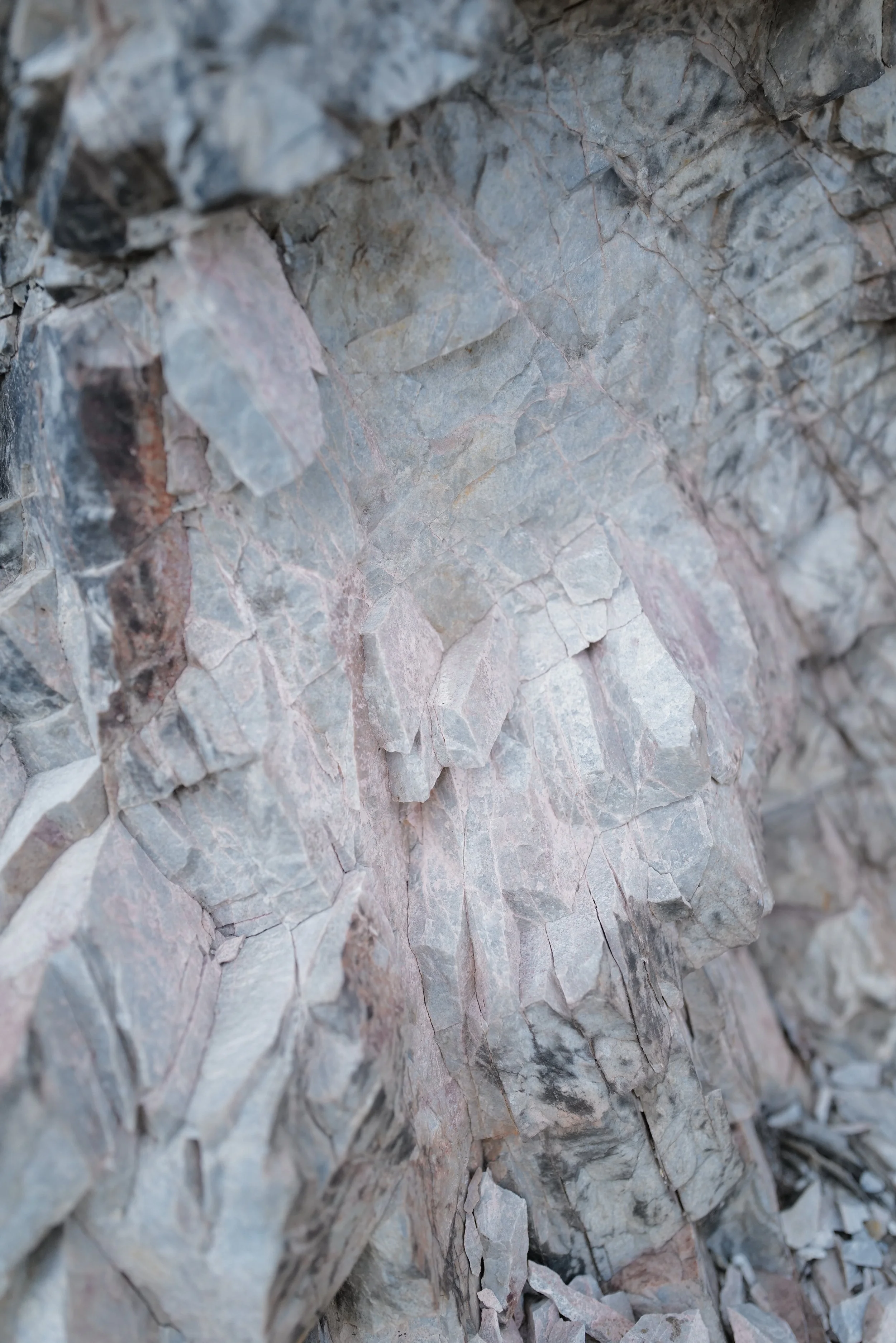 Close-up view of a rocky, uneven stone surface with cracks and various shades of gray and pink.