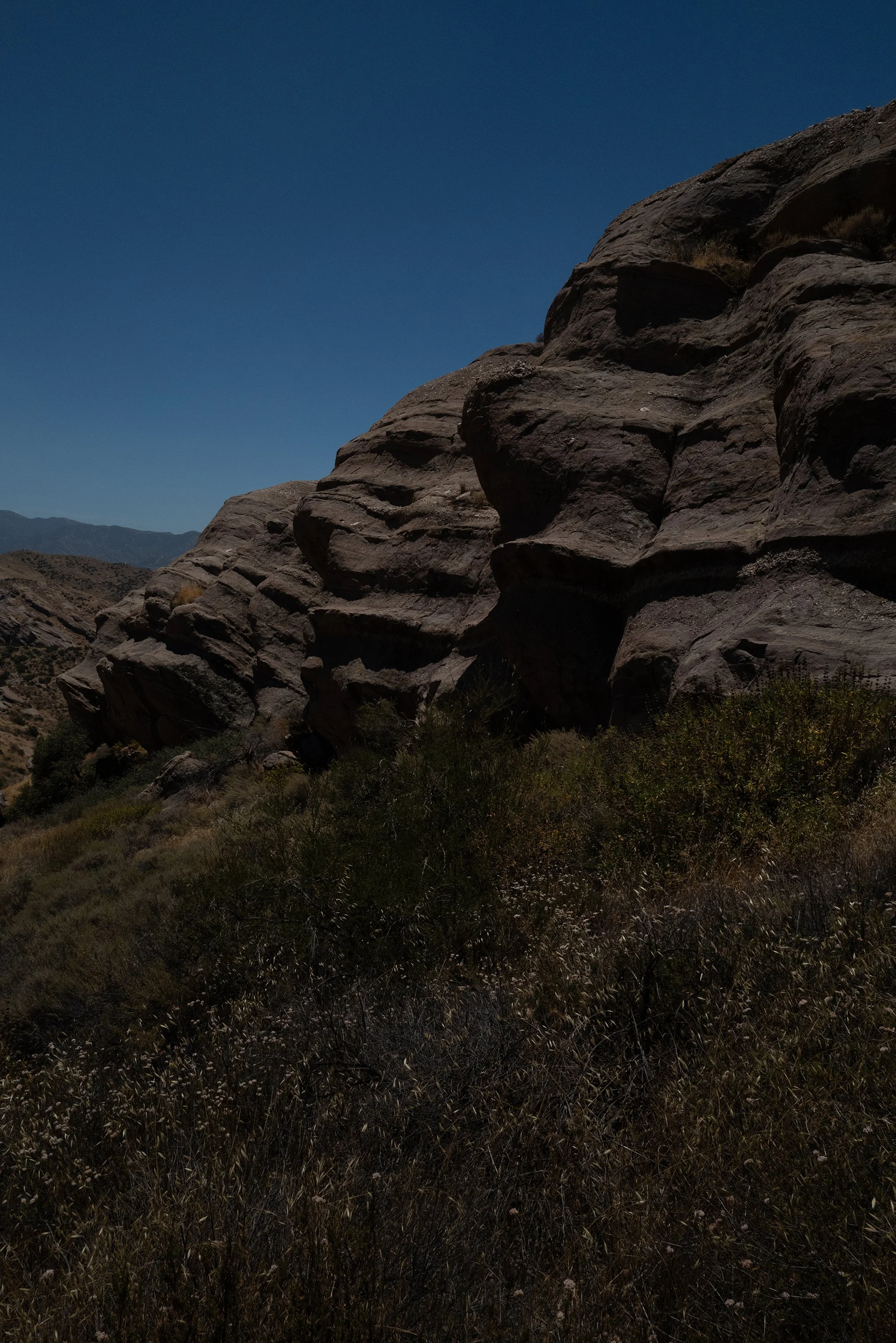 Large rock formation in a desert landscape with distant mountains under a clear blue sky.