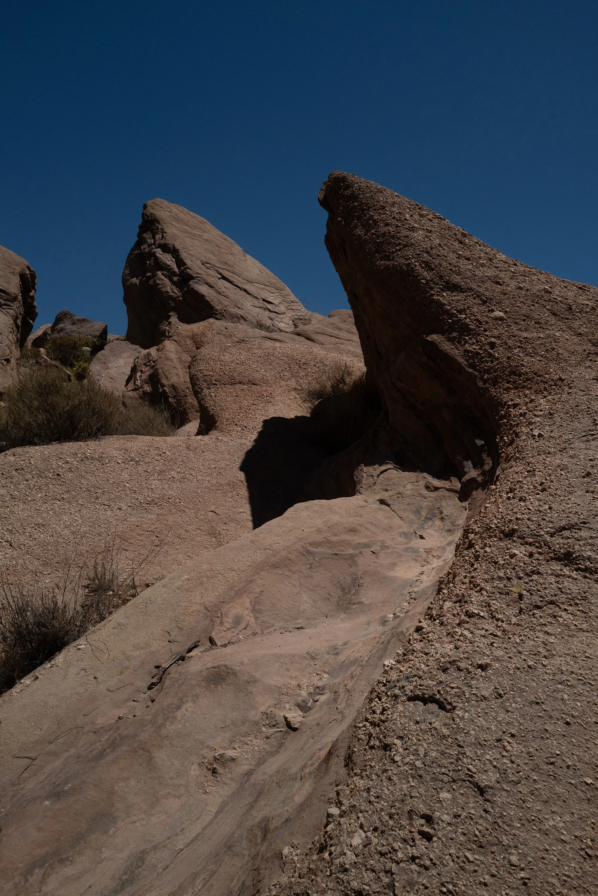 Desert landscape with large rocks and sparse vegetation under a clear blue sky.