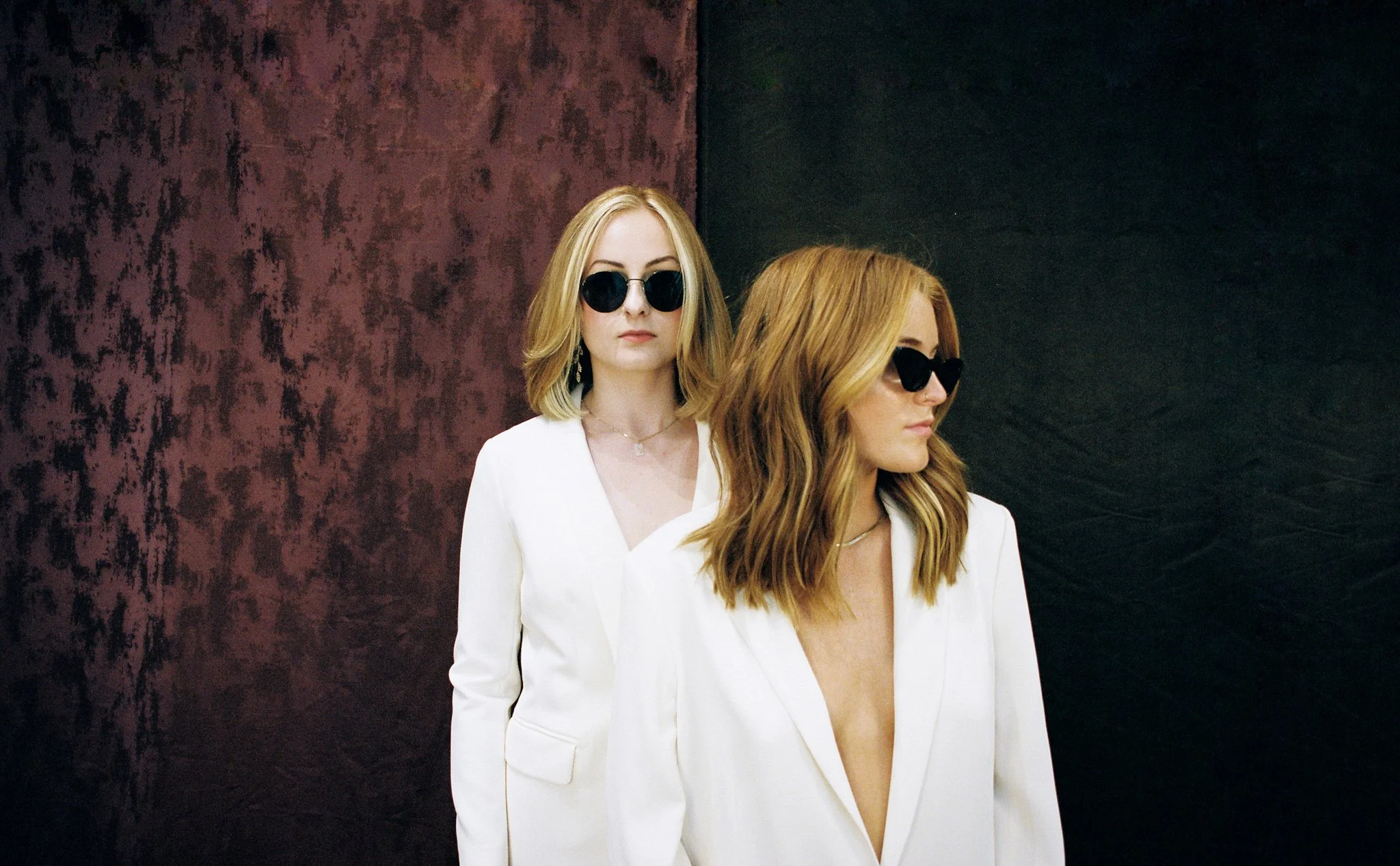 Two women in white suits and sunglasses looking in different directions.