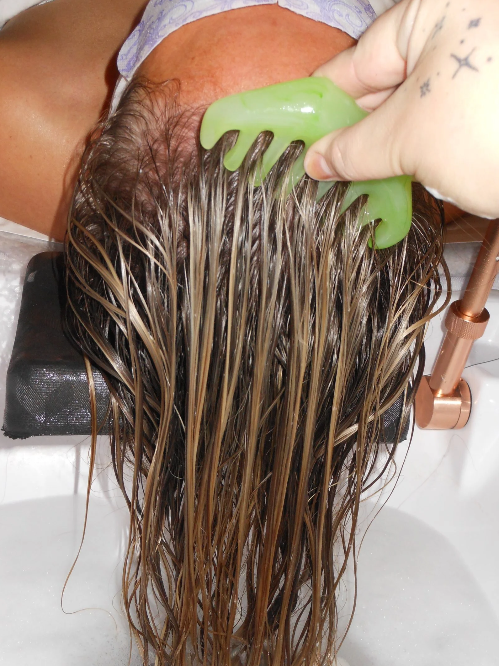 Green wide tooth comb brushing through brown hair.