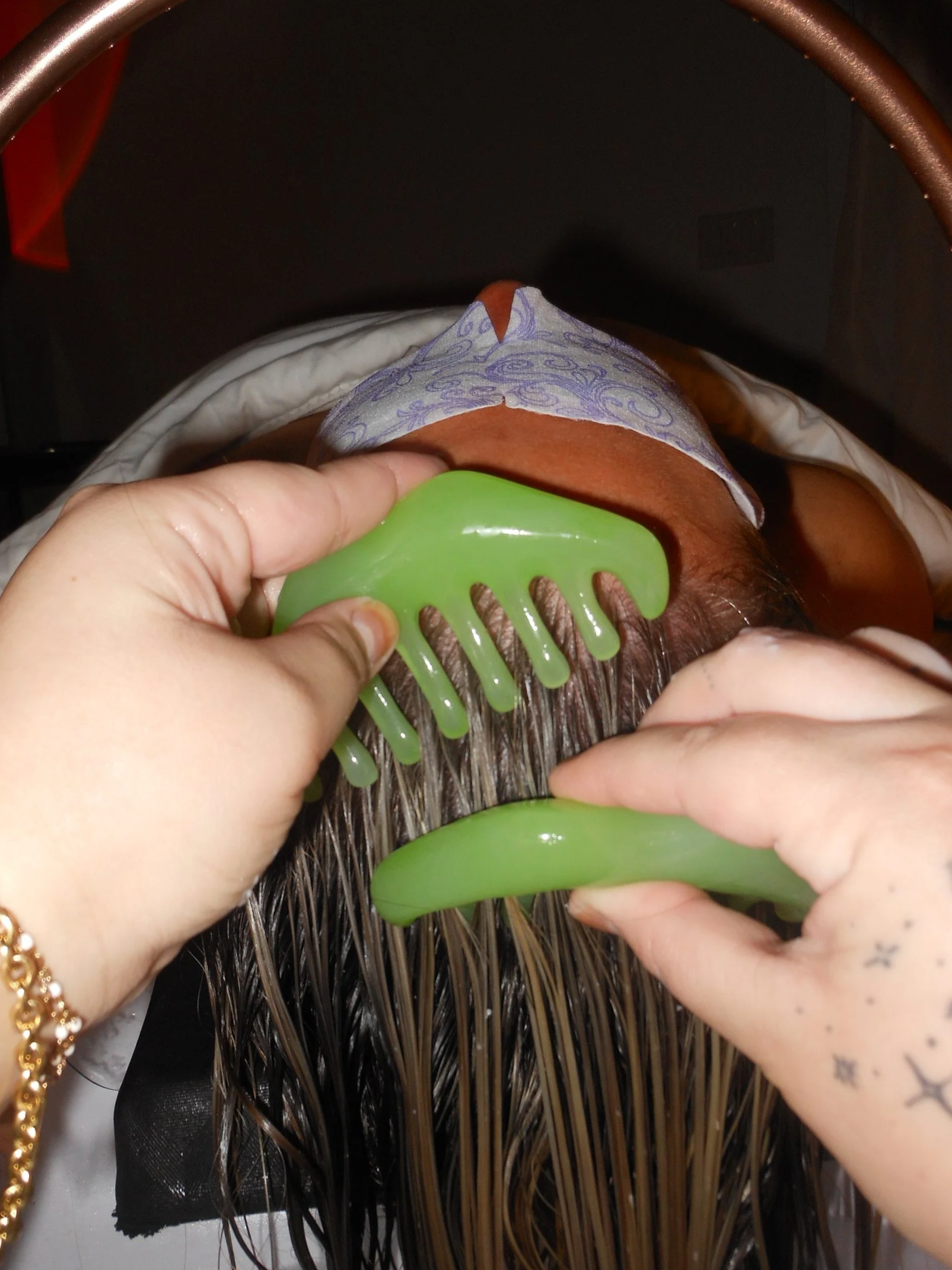 Two green combs being brushed through client's blonde hair.