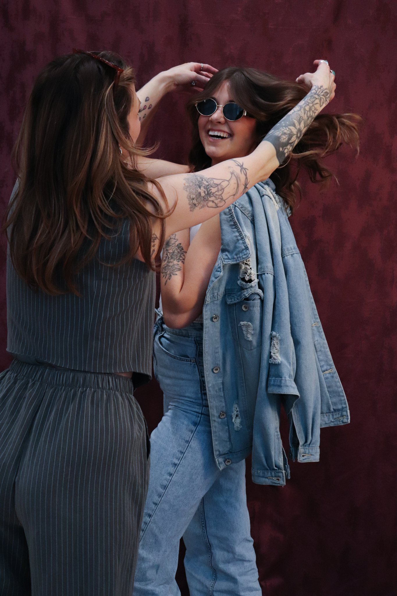 Woman with brown hair fixing the hair of another woman smiling with brown hair and sunglasses on.