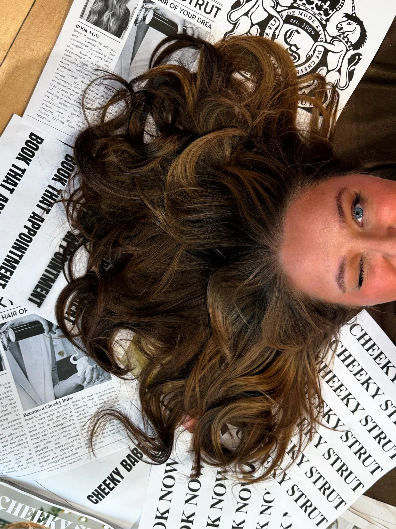 Woman laying on a pile of papers with her brown hair fanned out wink at the camera.