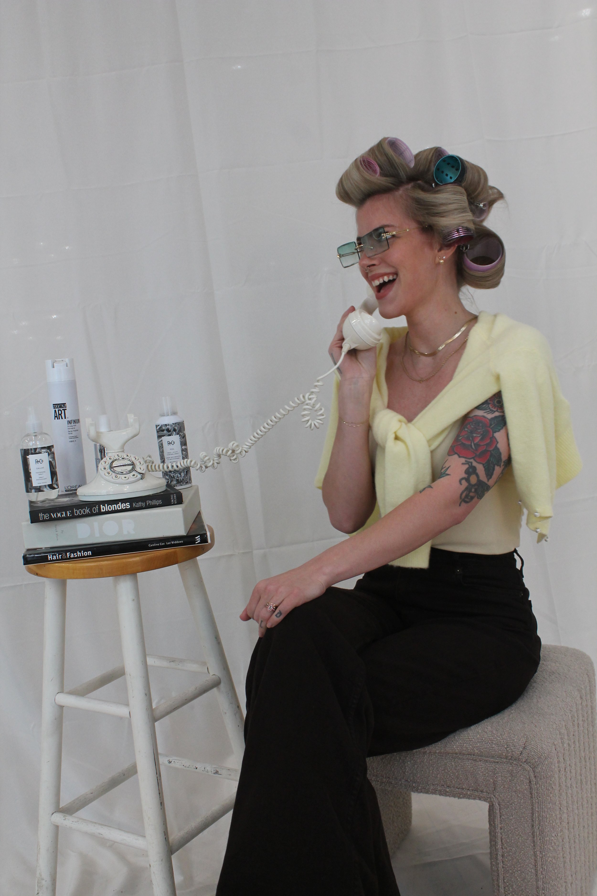 A girl with blonde hair and rollers in sitting and answering an old style phone.