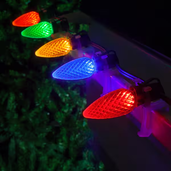 Close-up of multicolored LED Christmas lights, including red, yellow, green, blue, and purple bulbs, plugged into an extension cord on a dark background.