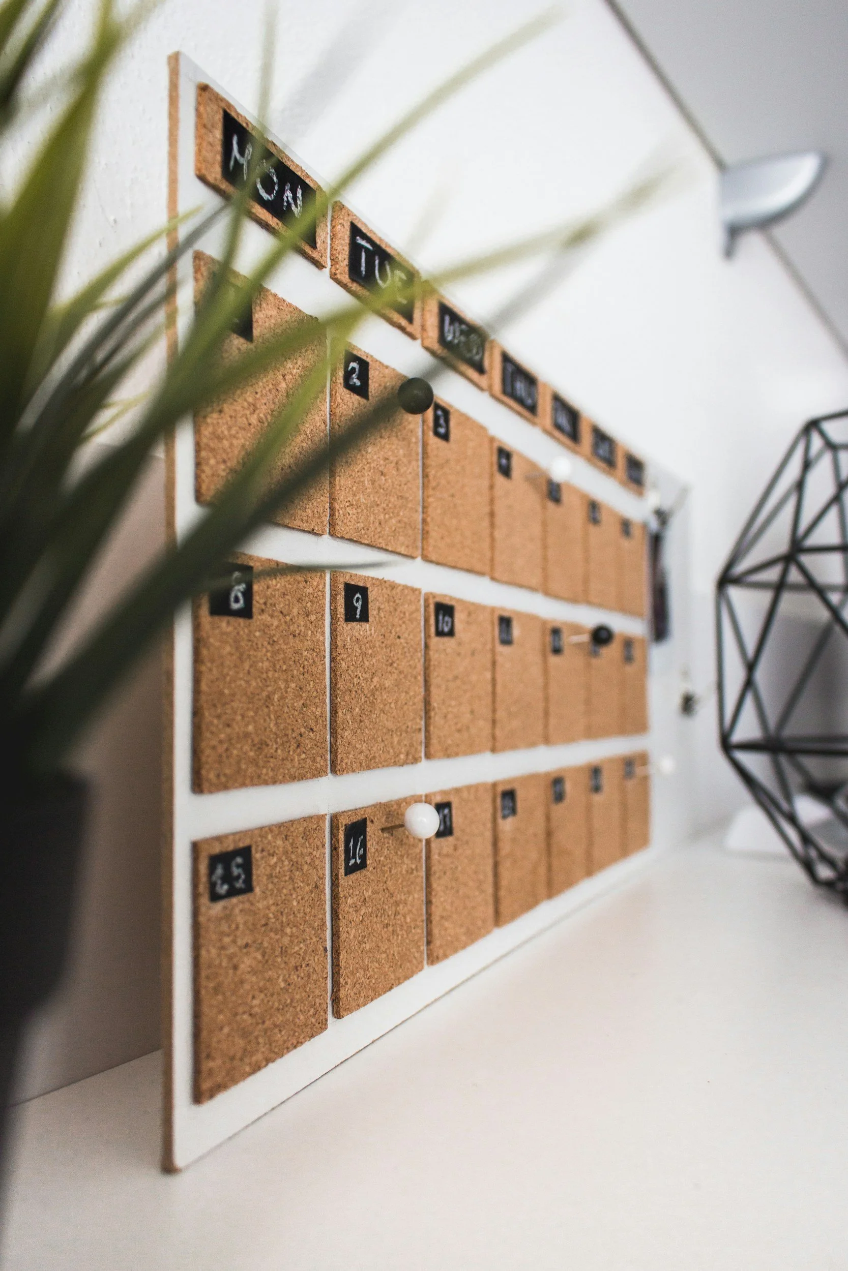 Corkboard calendar with Post-it notes and geometric decor on a white shelf