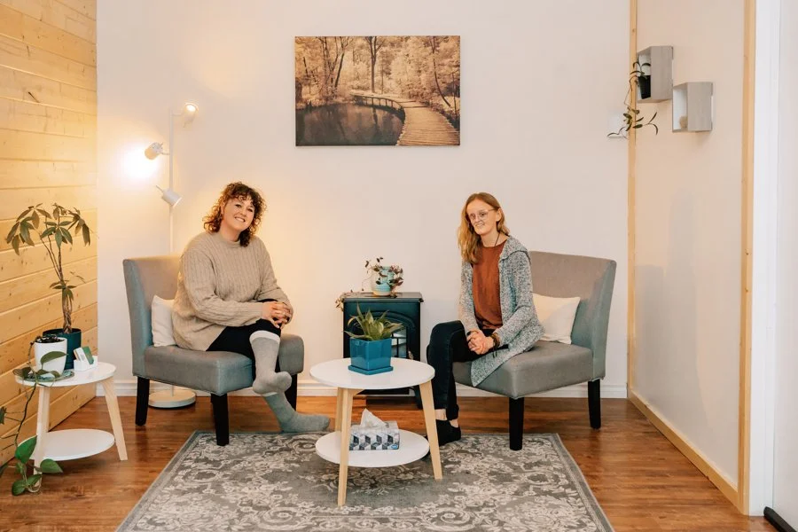 Two female health practitioners sitting in clinic, behind a small coffee table.