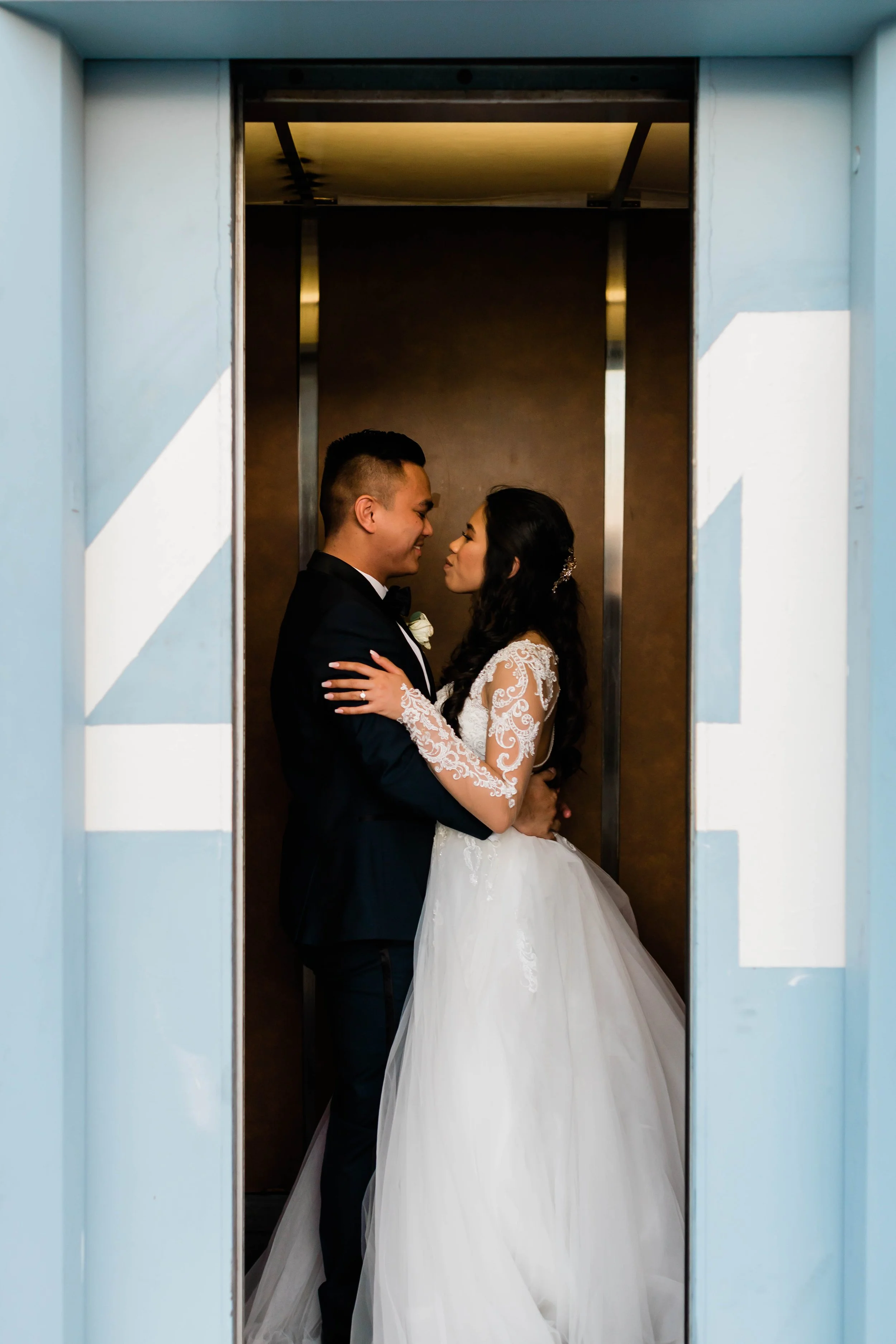 A bride and groom standing close inside an elevator, gazing into each other's eyes on their wedding day.