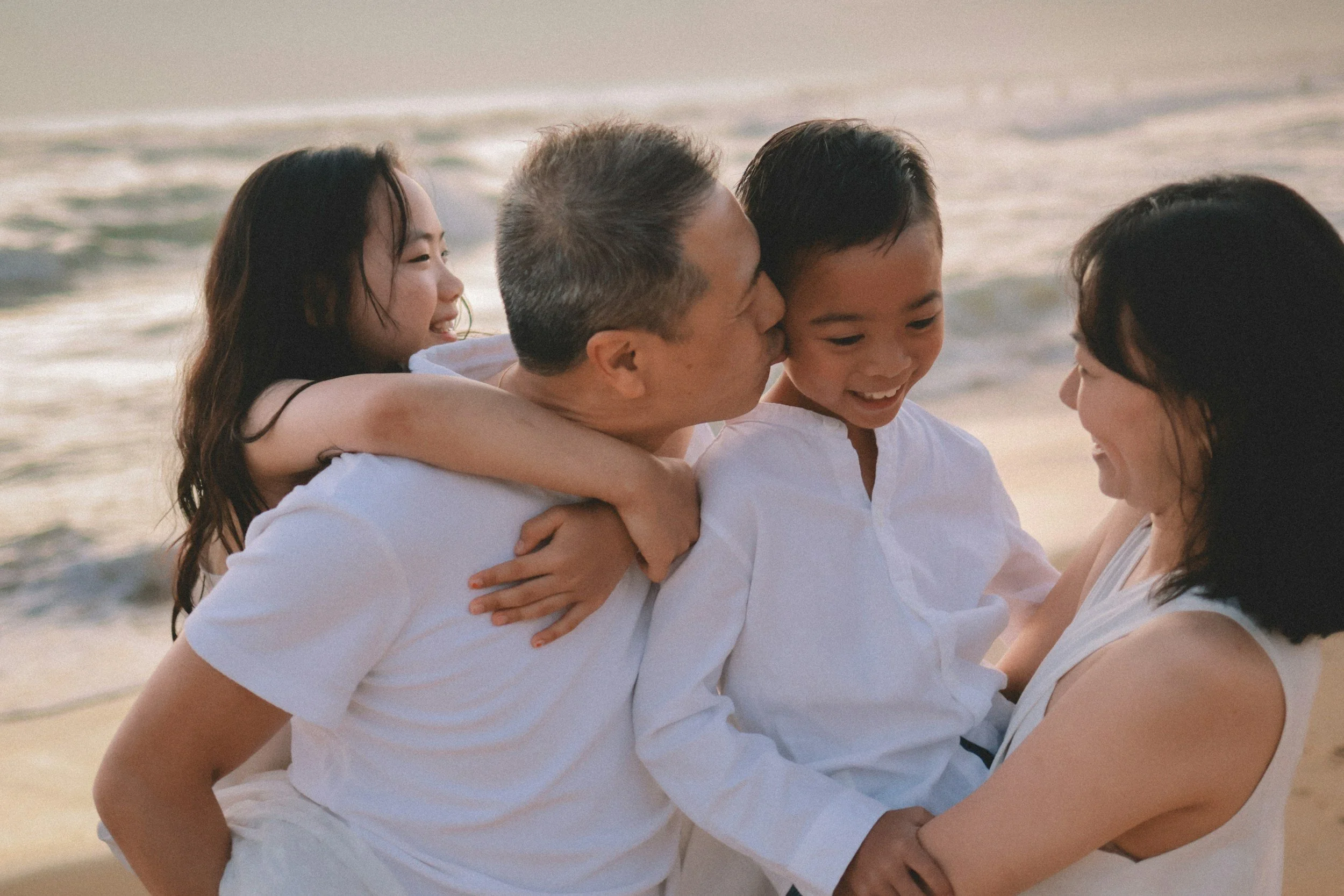 Family with two children at the beach, smiling and embracing each other.