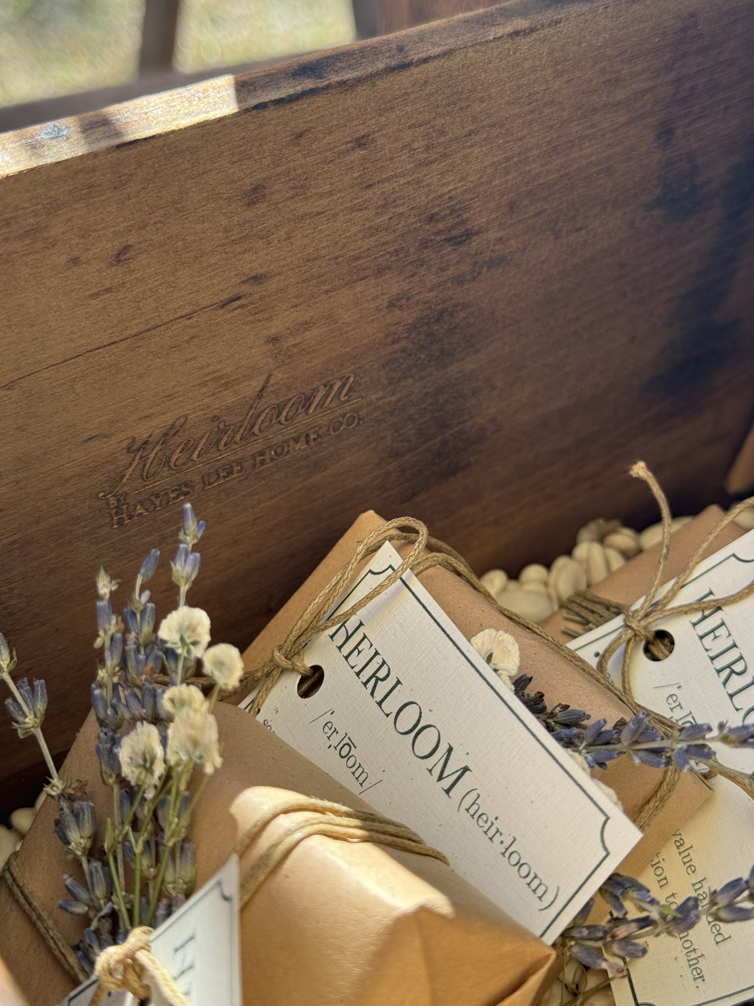 Wooden box containing wrapped packages tied with twine and adorned with dried lavender. Labels on the packages say "Heirloom" with its phonetic spelling.