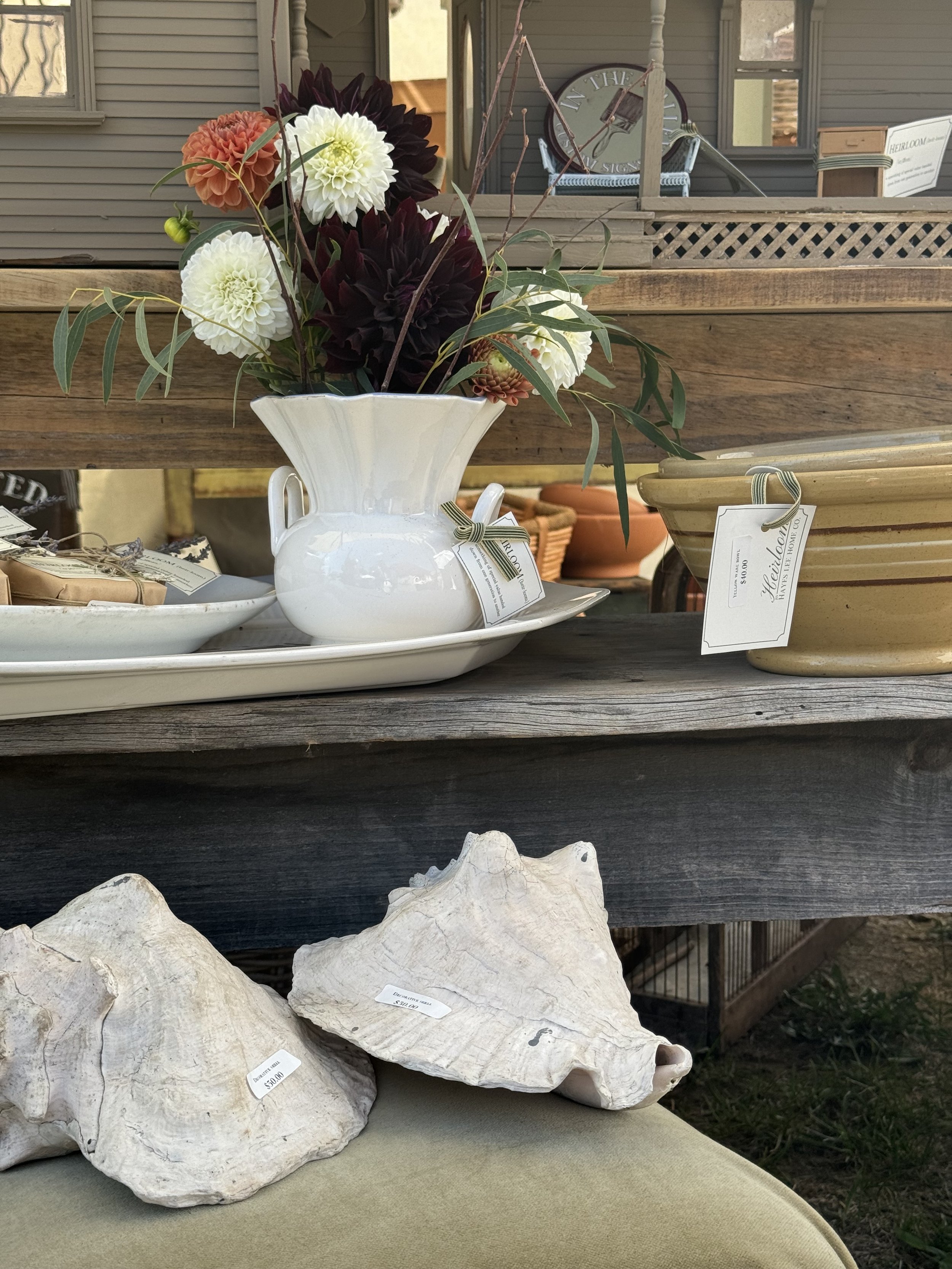 Decorative display featuring a white vase with flowers, conch shells, and various pottery items on wooden shelves.