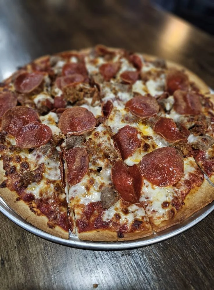 Pepperoni and sausage pizza on a metal tray with a wooden table background.