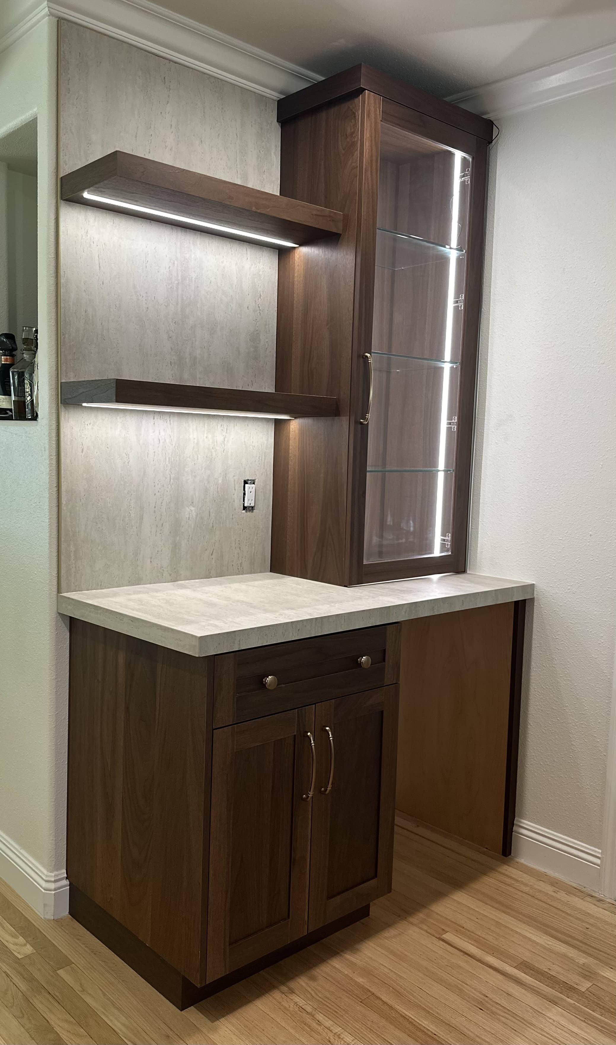 Modern kitchen bar with wooden cabinetry, glass display cabinet, open shelving, and integrated lighting.
