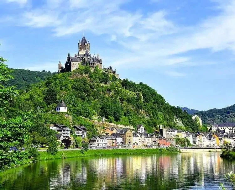 Medieval castle on a hill overlooking a river and a small town with colorful buildings