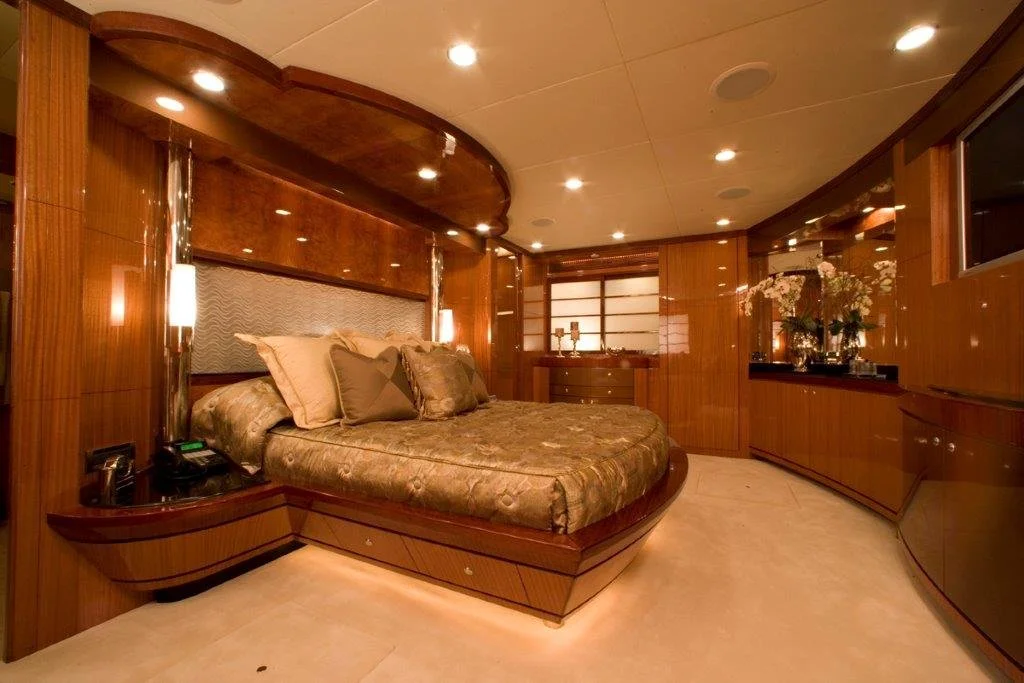 Luxurious yacht bedroom with a large bed, elegant wood paneling, ambient lighting, floral arrangements, and stylish decor.
