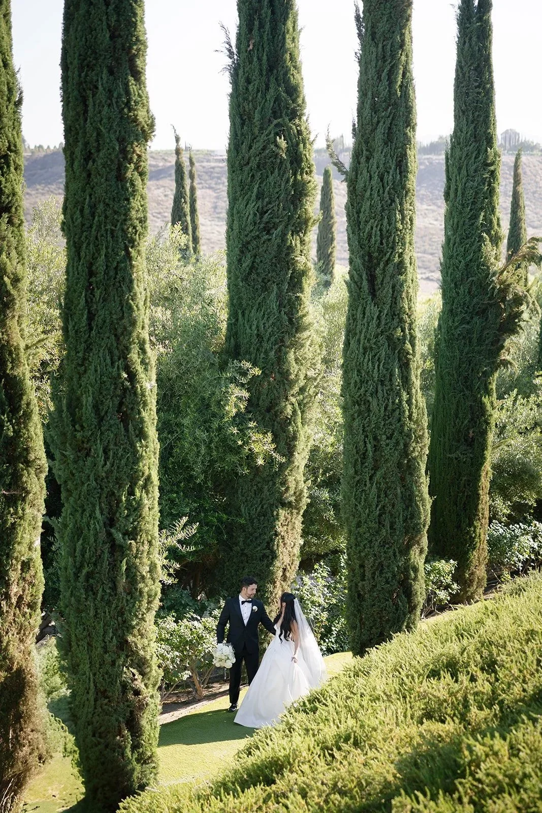 A romantic Southern California wedding moment designed and planned by Evermór Events, featuring an elegant outdoor ceremony setting among towering cypress trees.