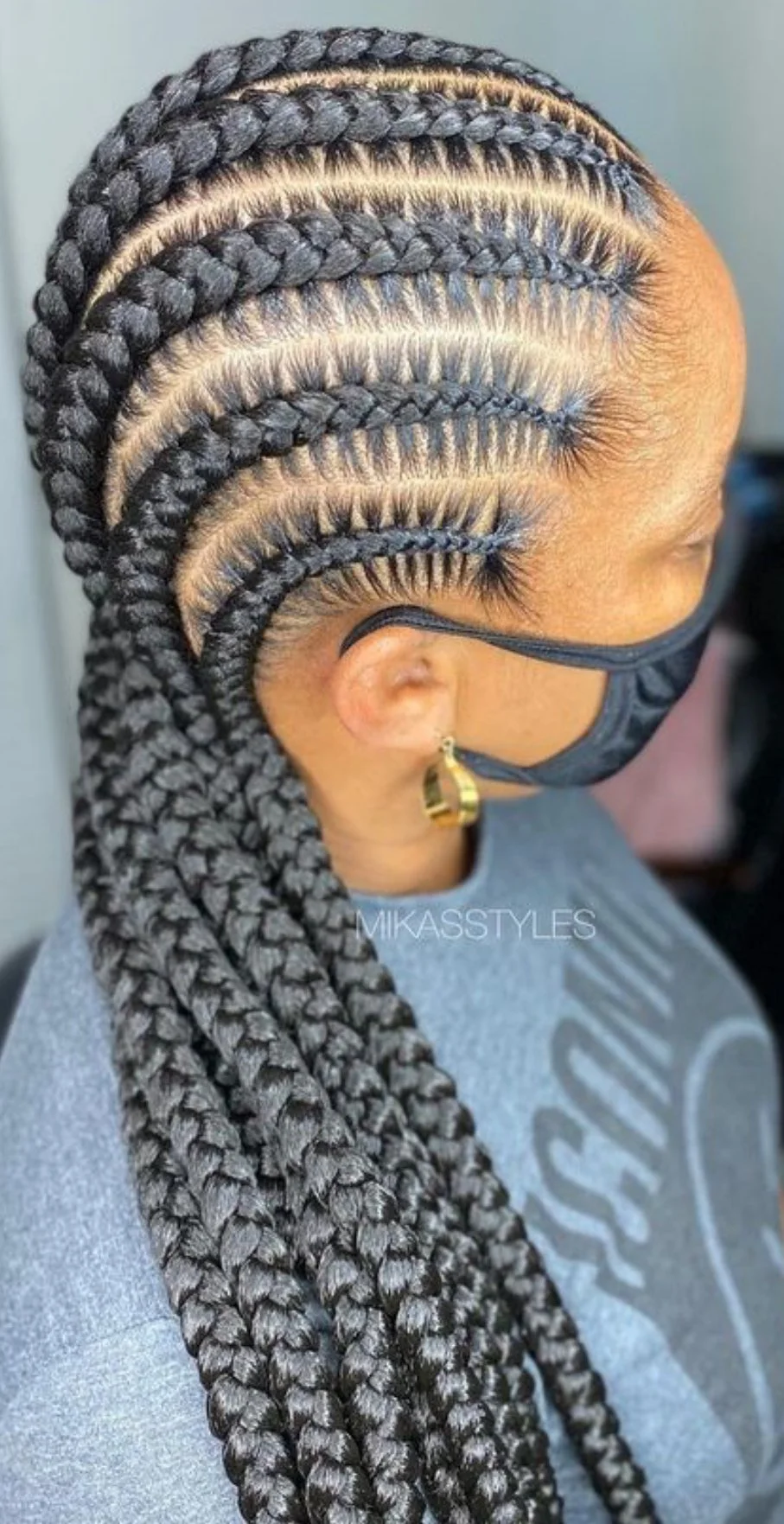Side view of a person with long, black, braided hair styled in neat cornrows, wearing a black face mask and gold hoop earrings.